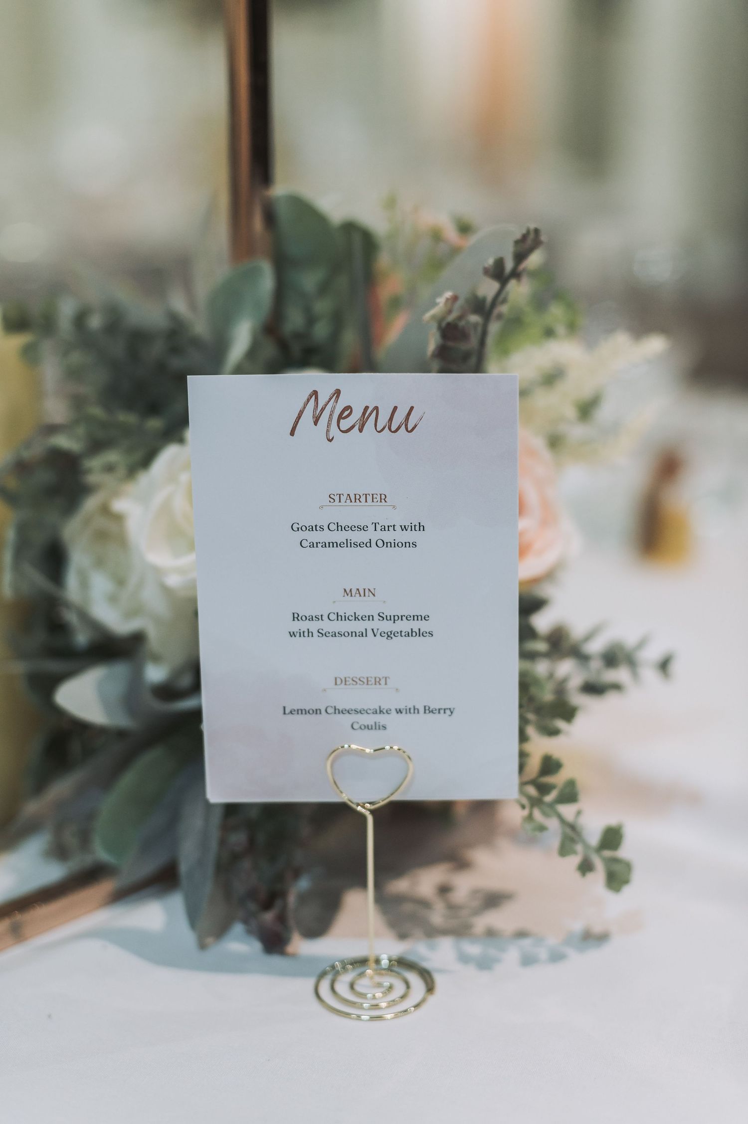 Wedding menu card displayed with eucalyptus and floral decor on white tablecloth.