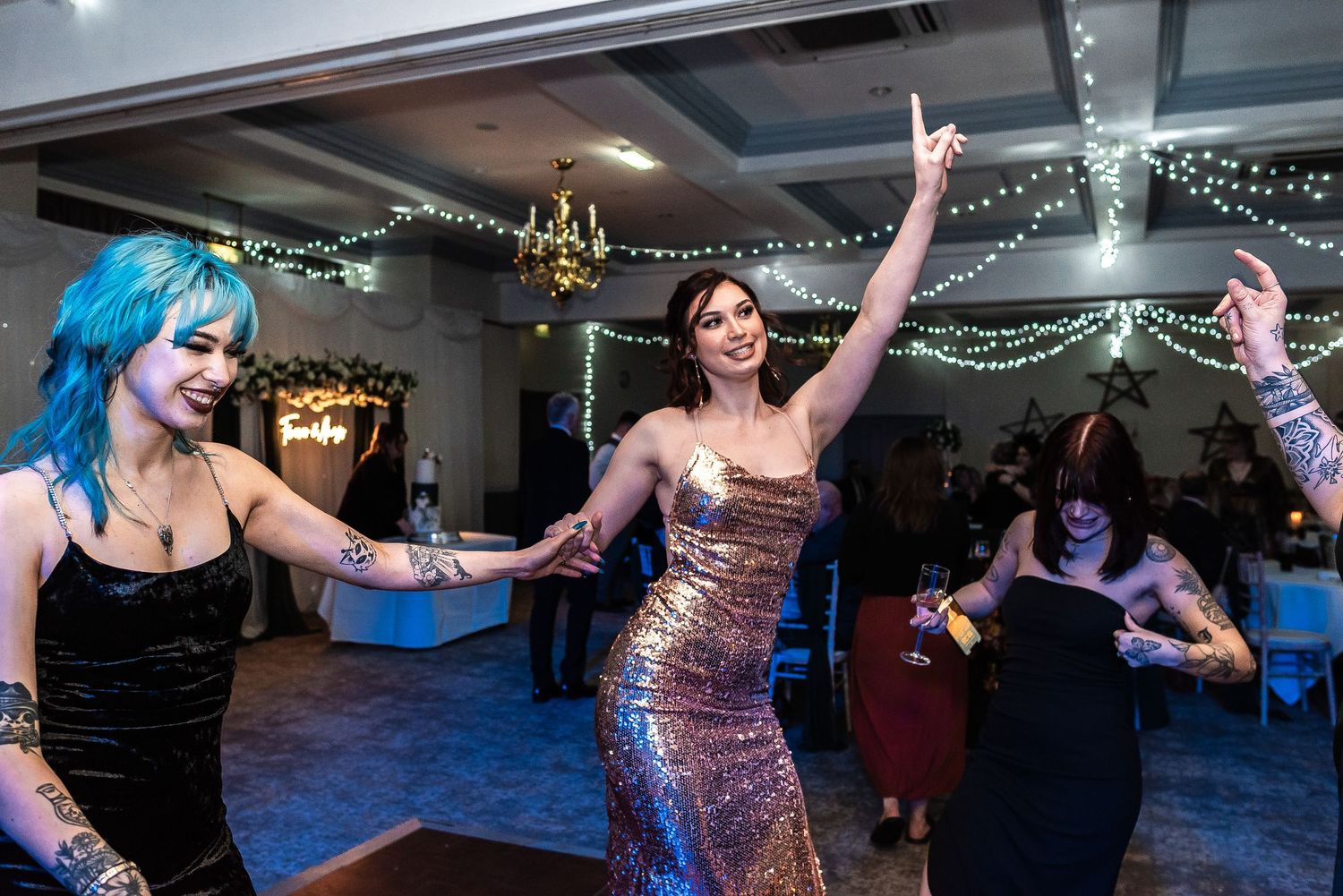 Party guests dancing energetically on illuminated dance floor at wedding reception.