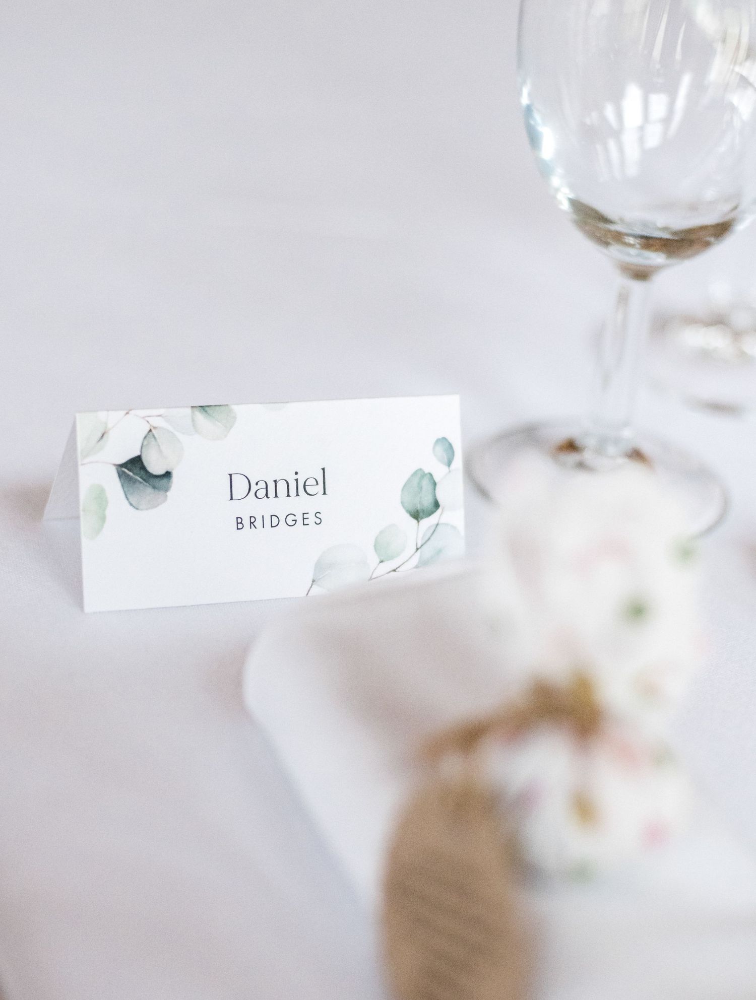 Minimalist wedding place card with delicate floral design beside stemware.