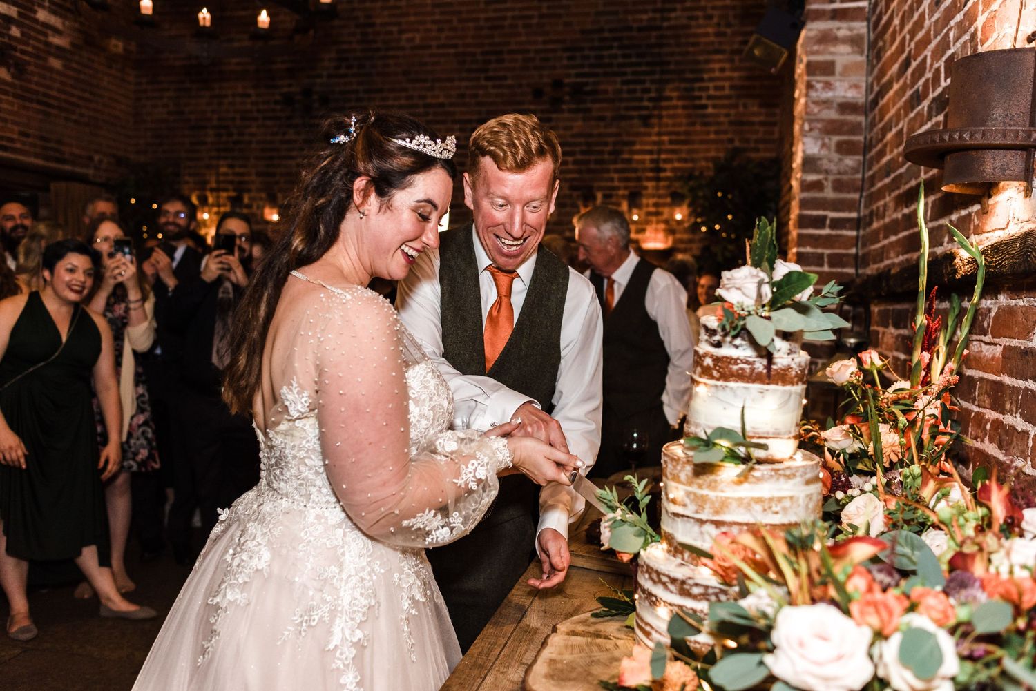 Couple cutting their elegant wedding cake at their reception with guests in background.