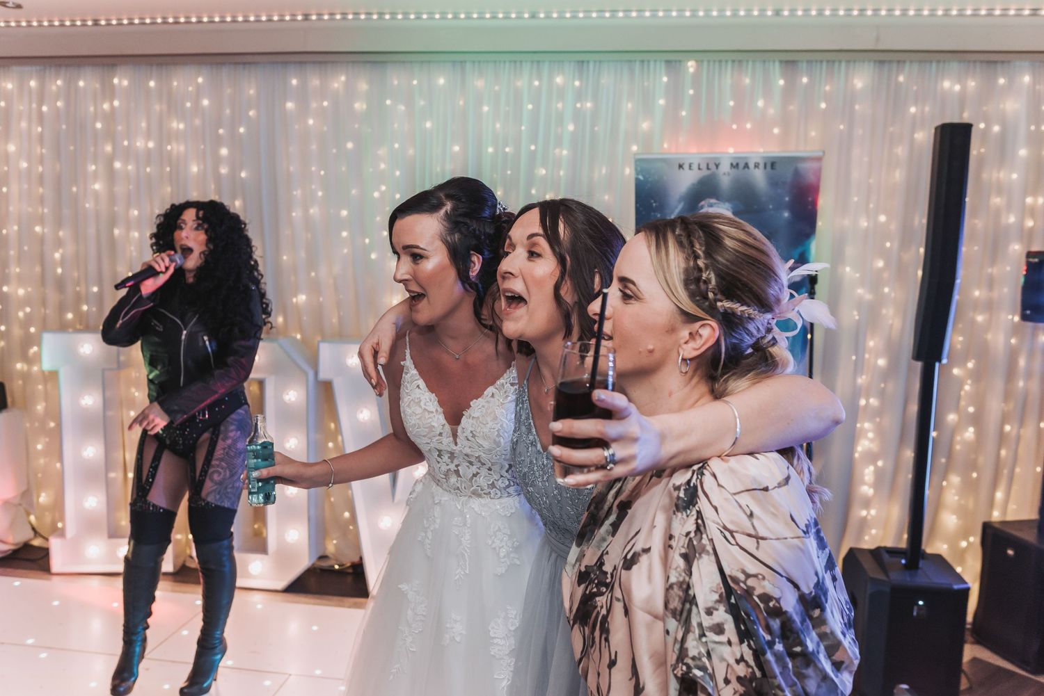 Energetic dancing and celebration at wedding reception with sparkly backdrop.