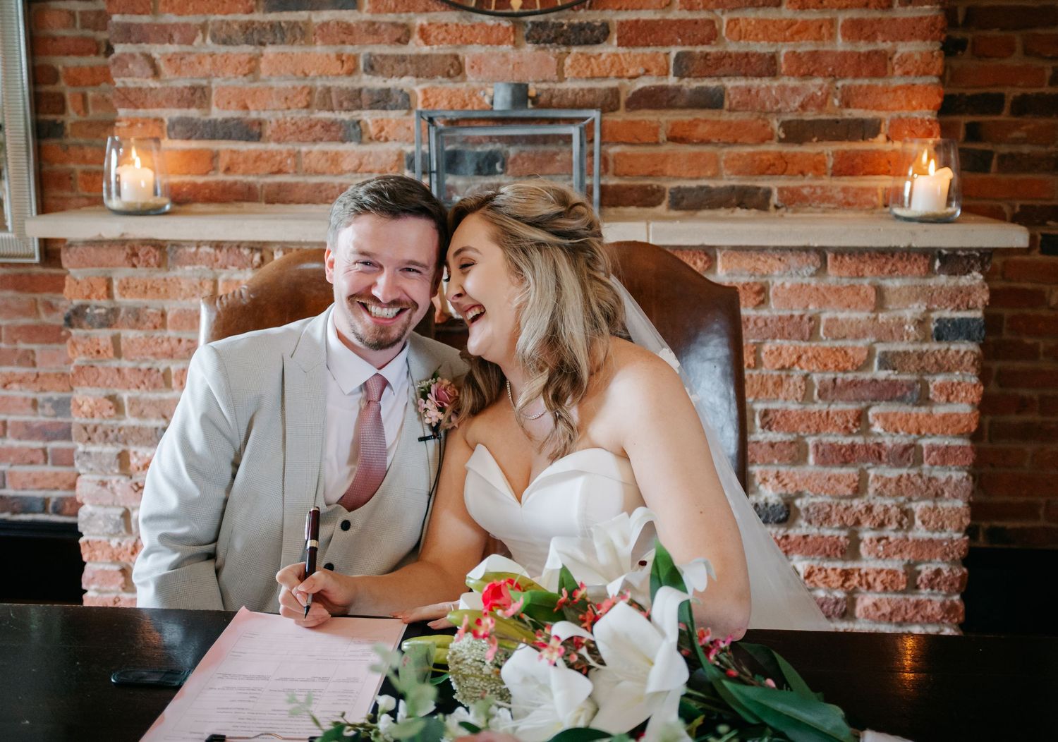 A romantic wedding reception scene at a rustic brick-walled venue with table decorations and floral centerpieces.