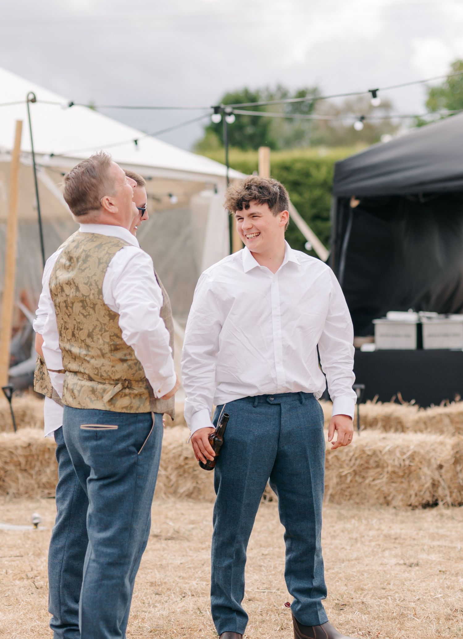 Two people in white shirts and jeans share a candid moment of laughter while standing on hay bales at an outdoor event.