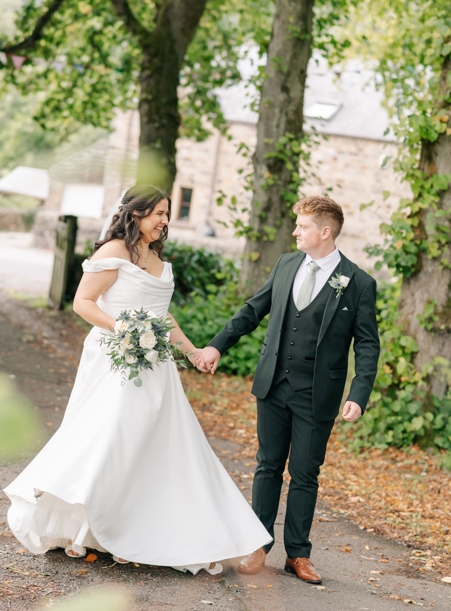 Wedding couple walking and dancing along a tree-lined path.
