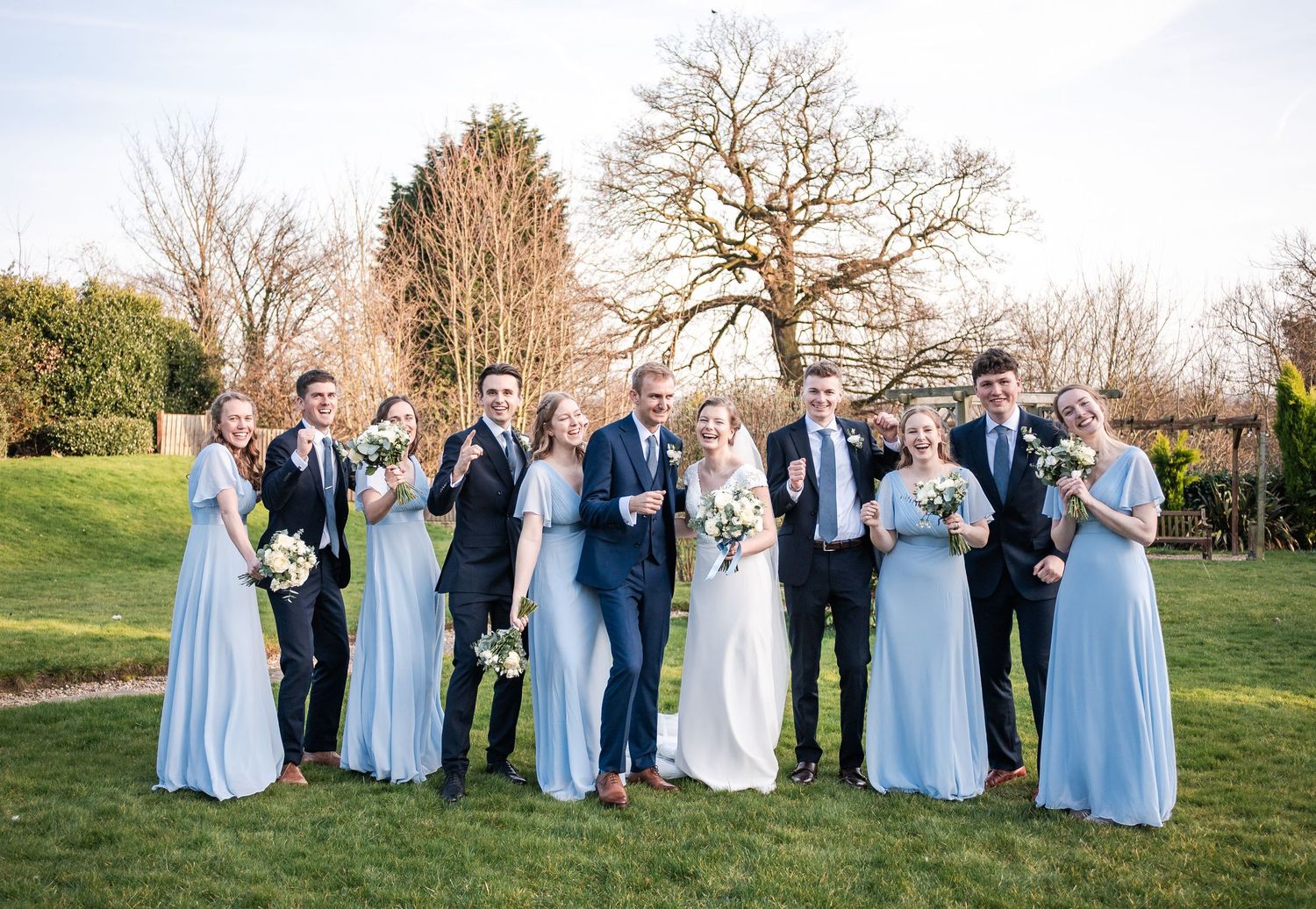 Wedding party in light blue dresses and navy suits posed together outdoors.