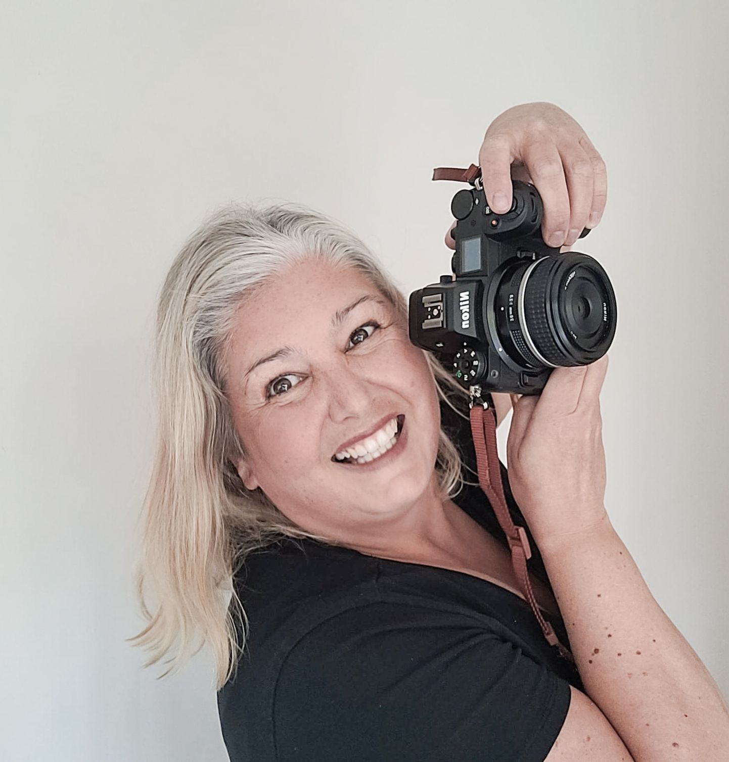 Professional photographer with blonde hair wearing black shirt holding DSLR camera against white background.