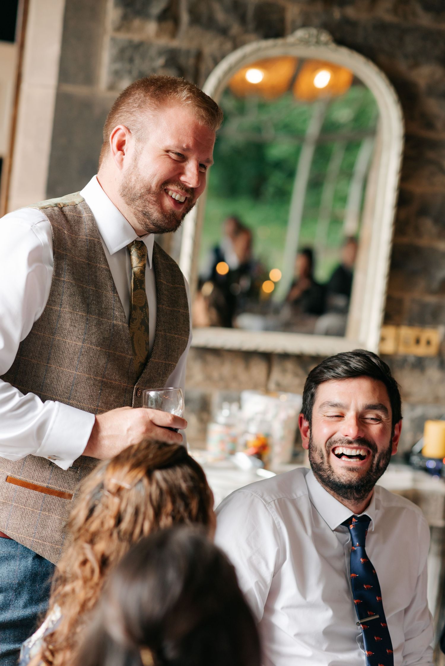 Candid moments of laughter and conversation during wedding toasts at a rustic venue.