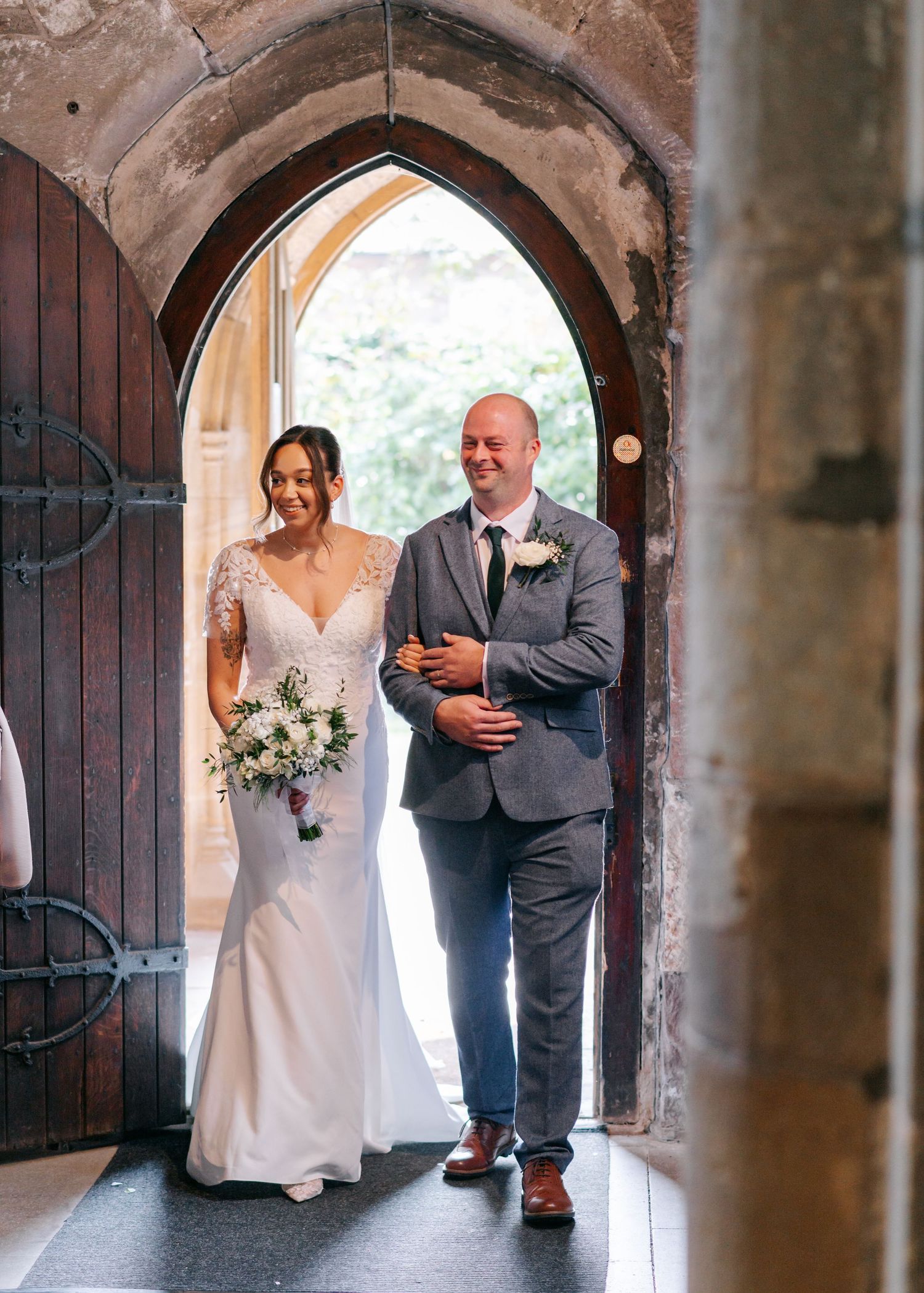 Wedding couple walking through a historic stone archway in a church corridor.