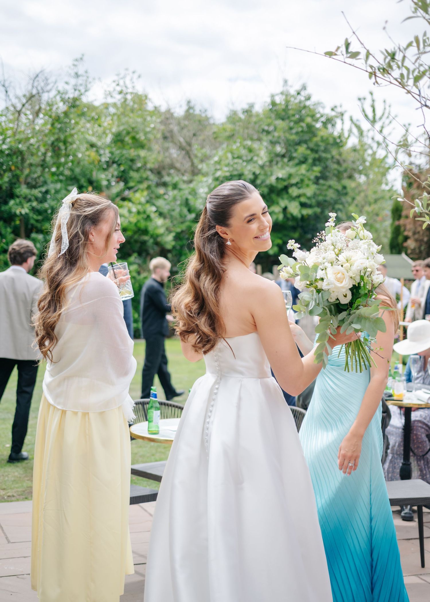 Wedding party members in light yellow and turquoise dresses dance together at an outdoor reception celebration.