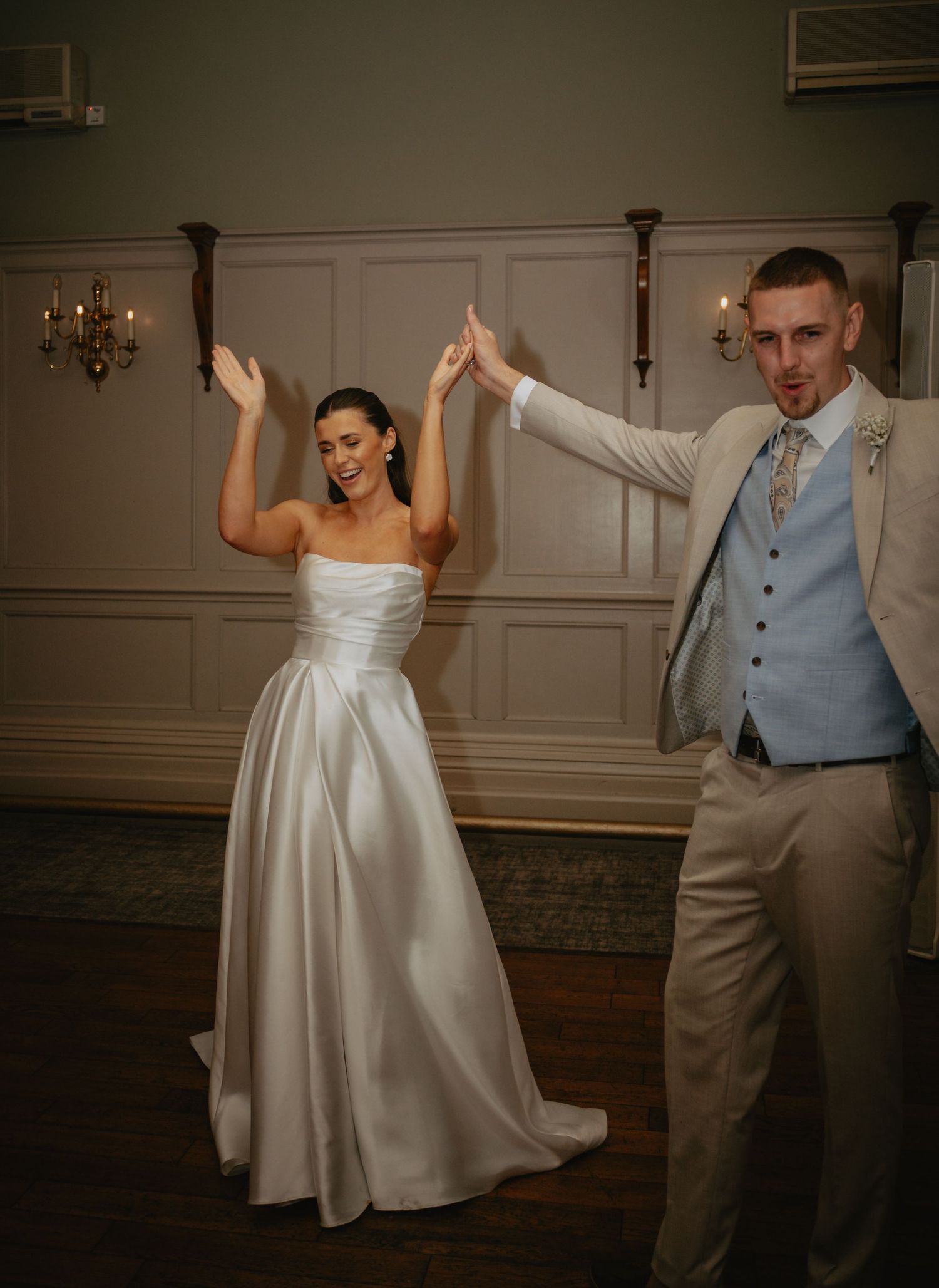 A joyful couple dancing and raising their hands during their wedding reception in an elegant ballroom.