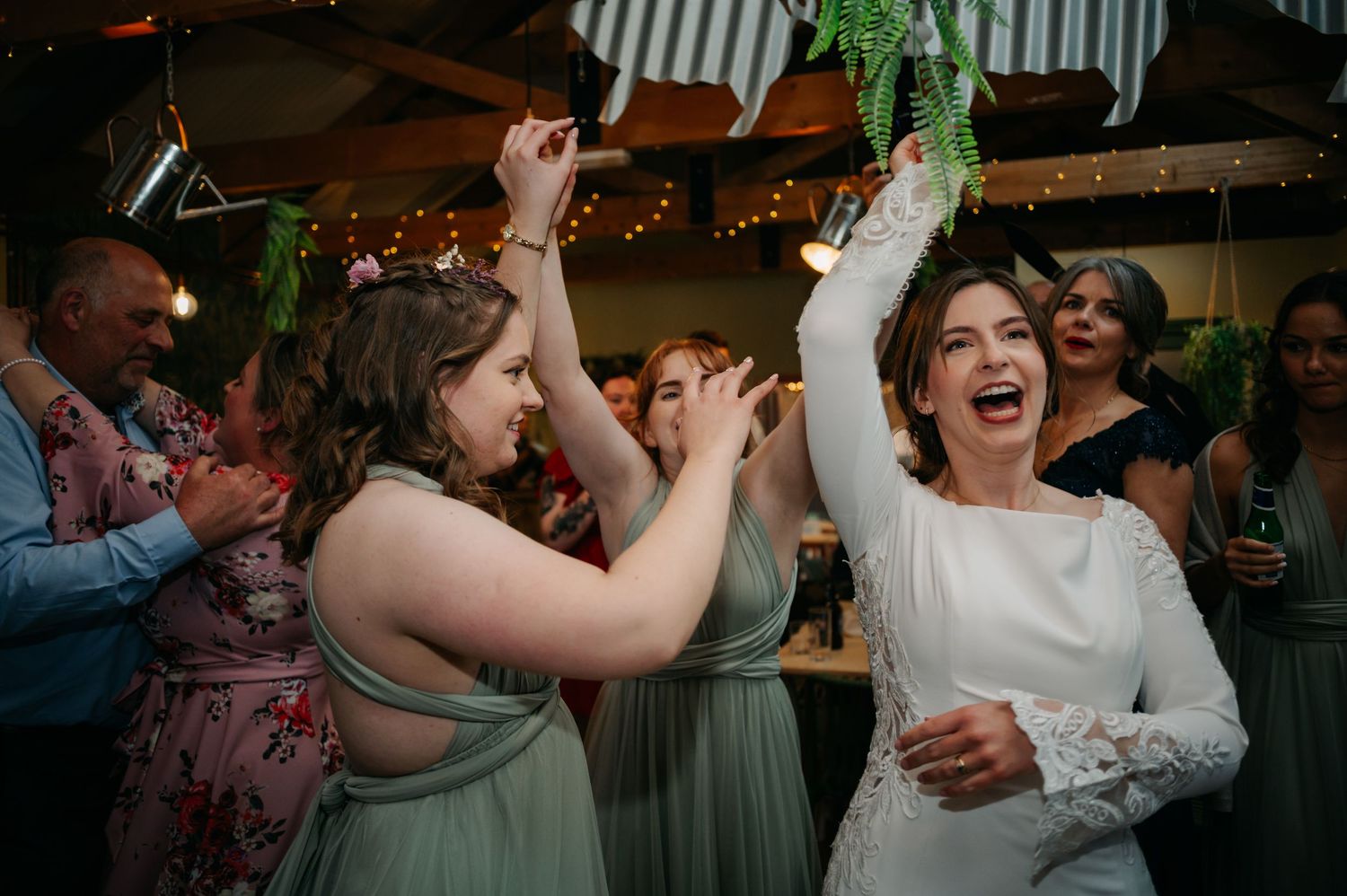 Wedding reception guests dancing and celebrating with joyful expressions under string lights.