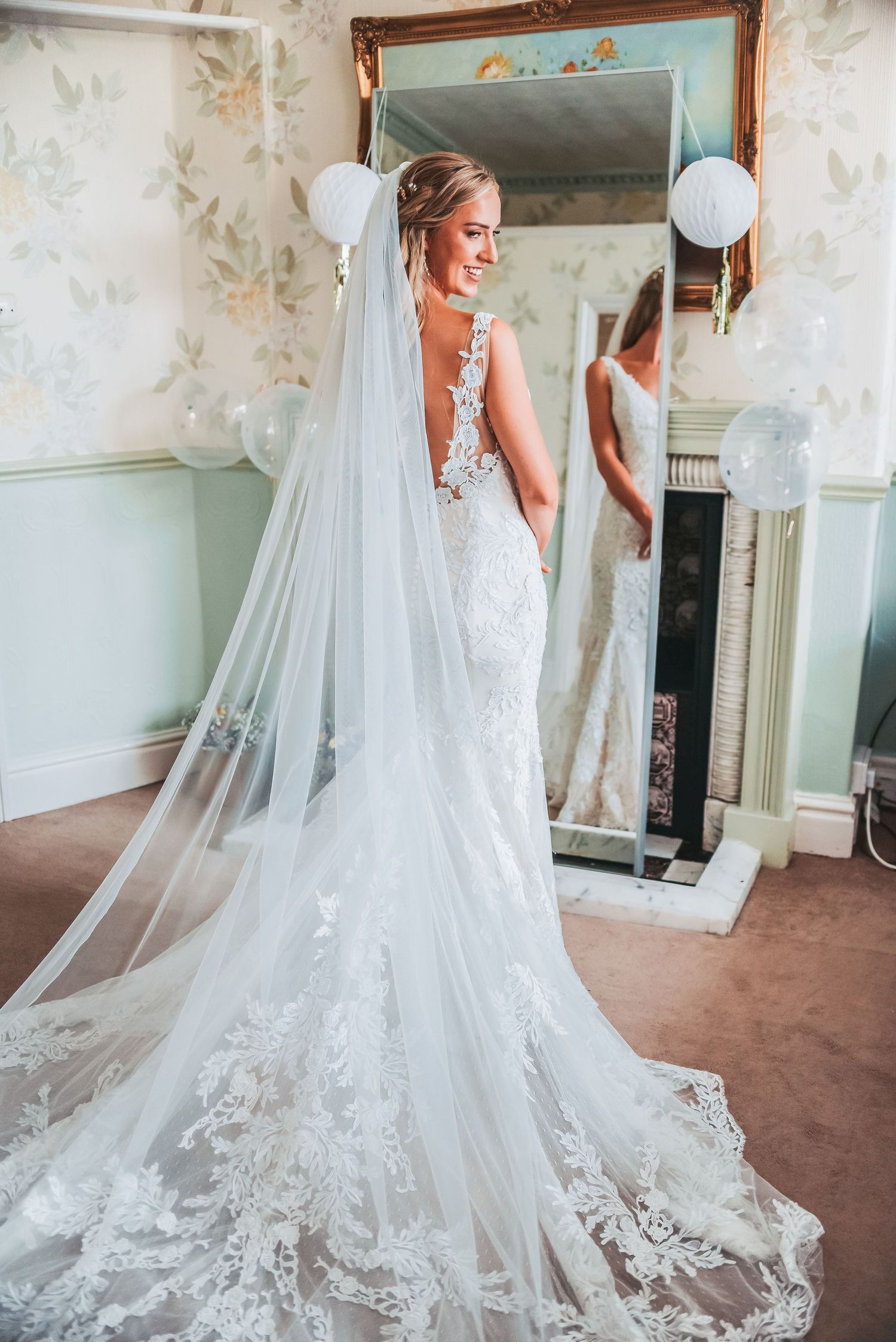 Elegant lace wedding dress with cathedral veil shown from behind in a vintage-style dressing room.