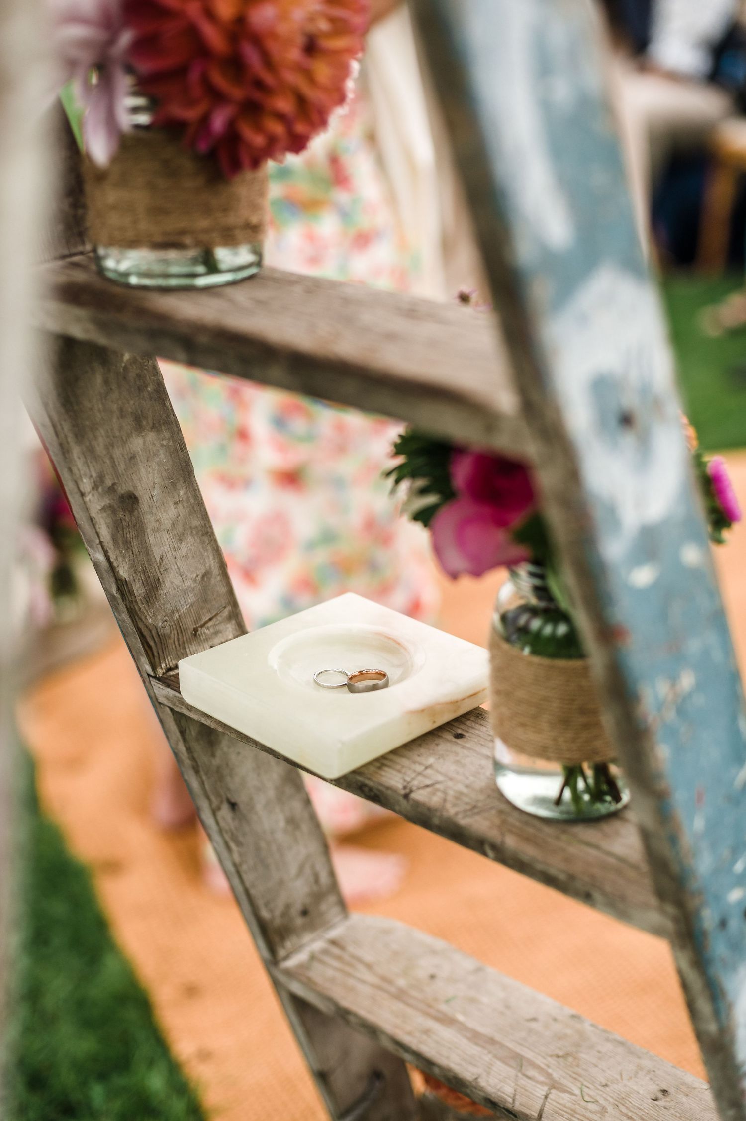 Wedding rings displayed on vintage wooden ladder with floral decorations.
