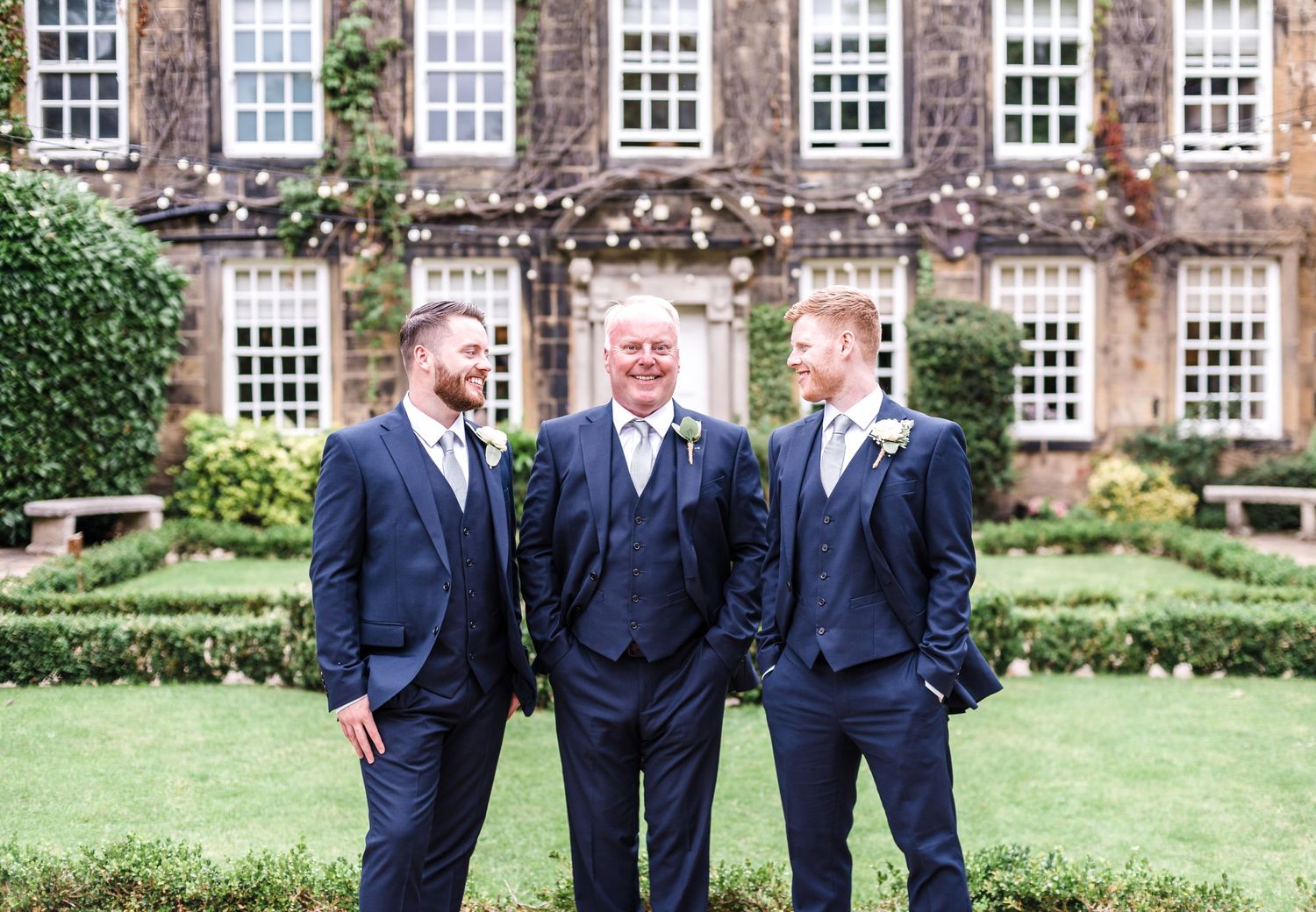 Three people in navy suits pose in front of an ivy-covered building.