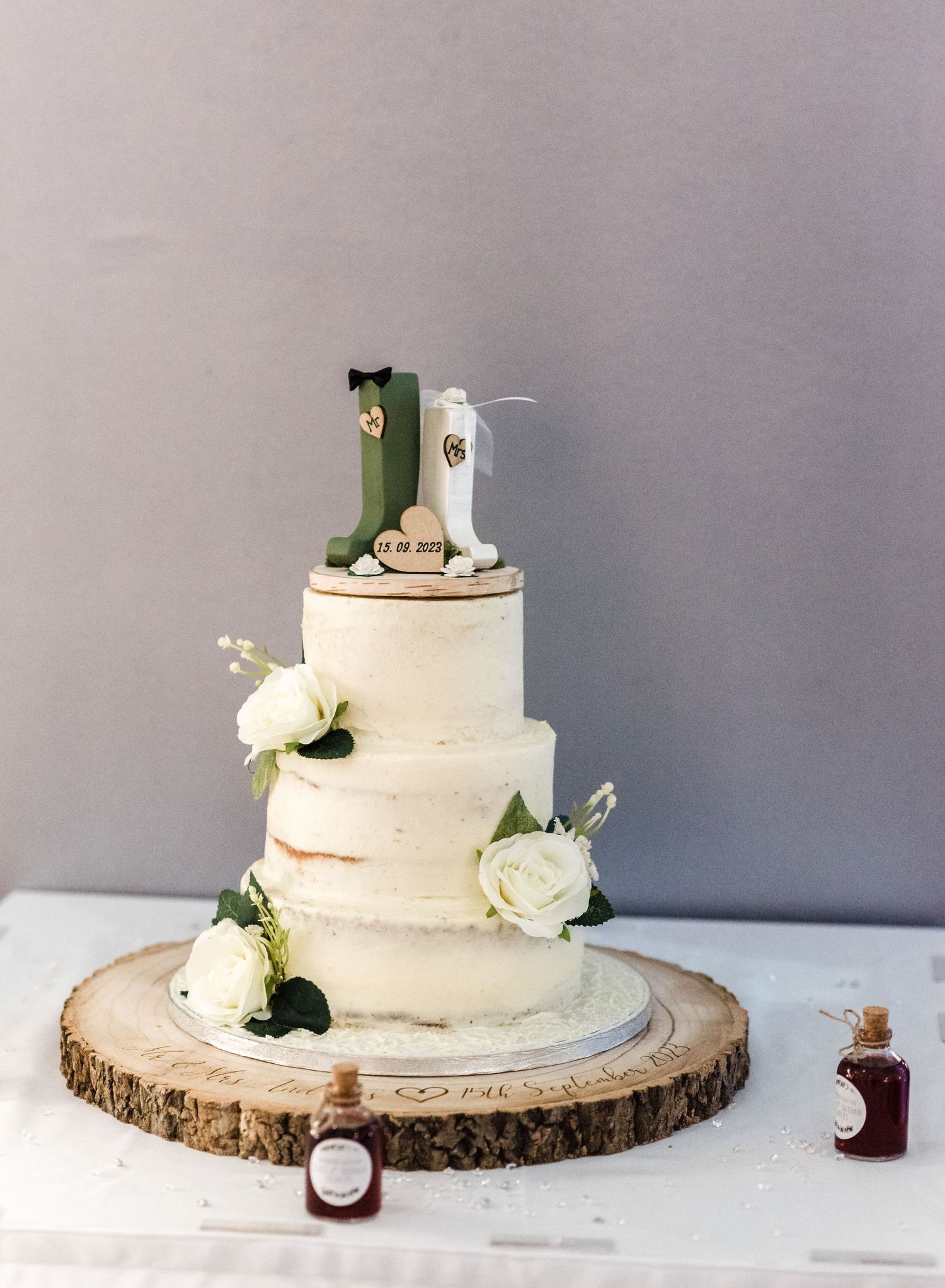 Three-tiered semi-naked wedding cake with white roses on a rustic wood slice base.