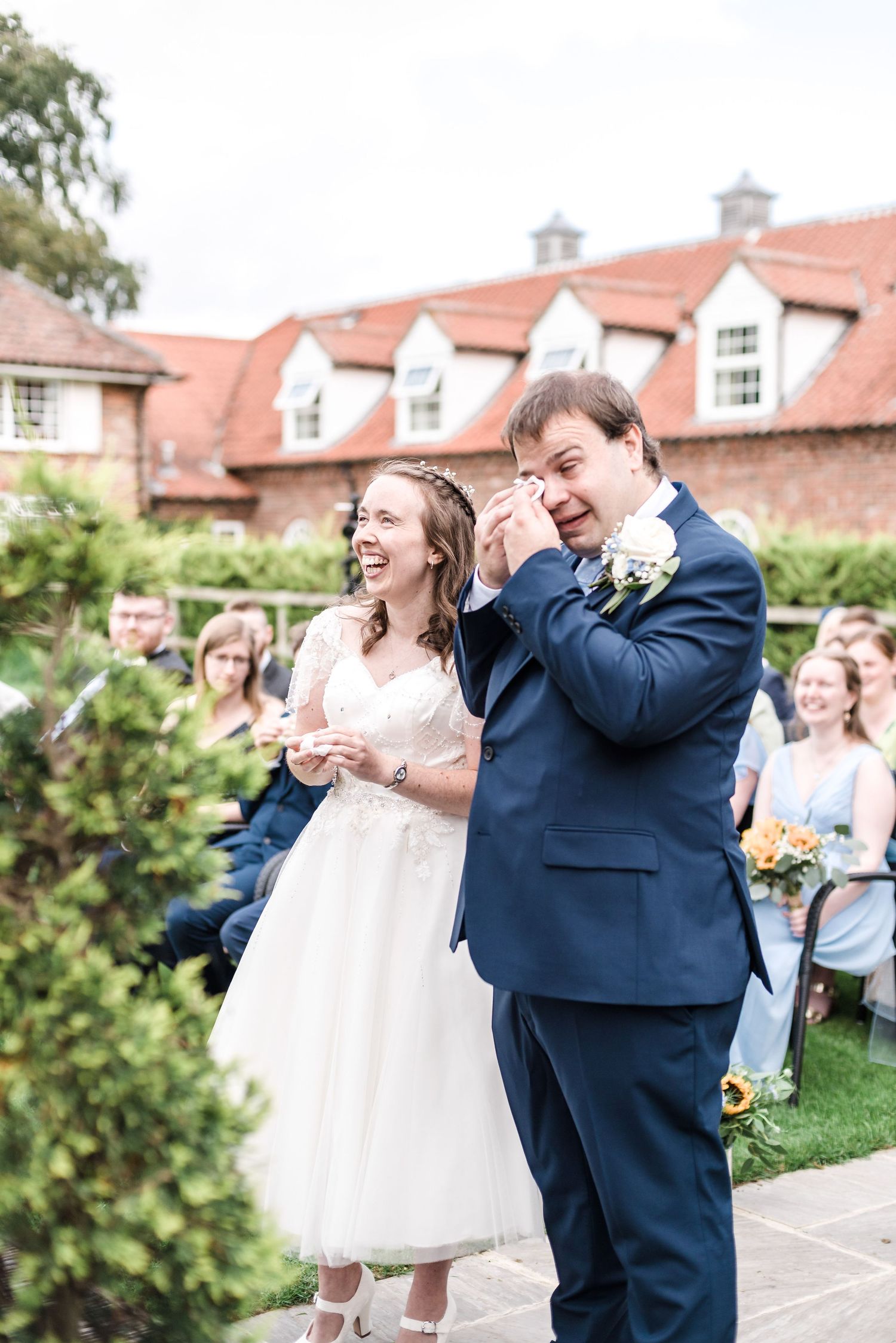 An emotional moment captured during an outdoor wedding ceremony with red-roofed buildings in the background.
