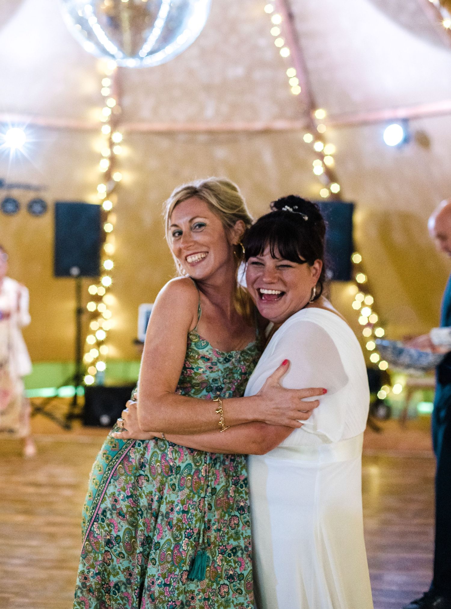 Two guests sharing a joyful embrace on the dance floor at a celebration with string lights overhead.