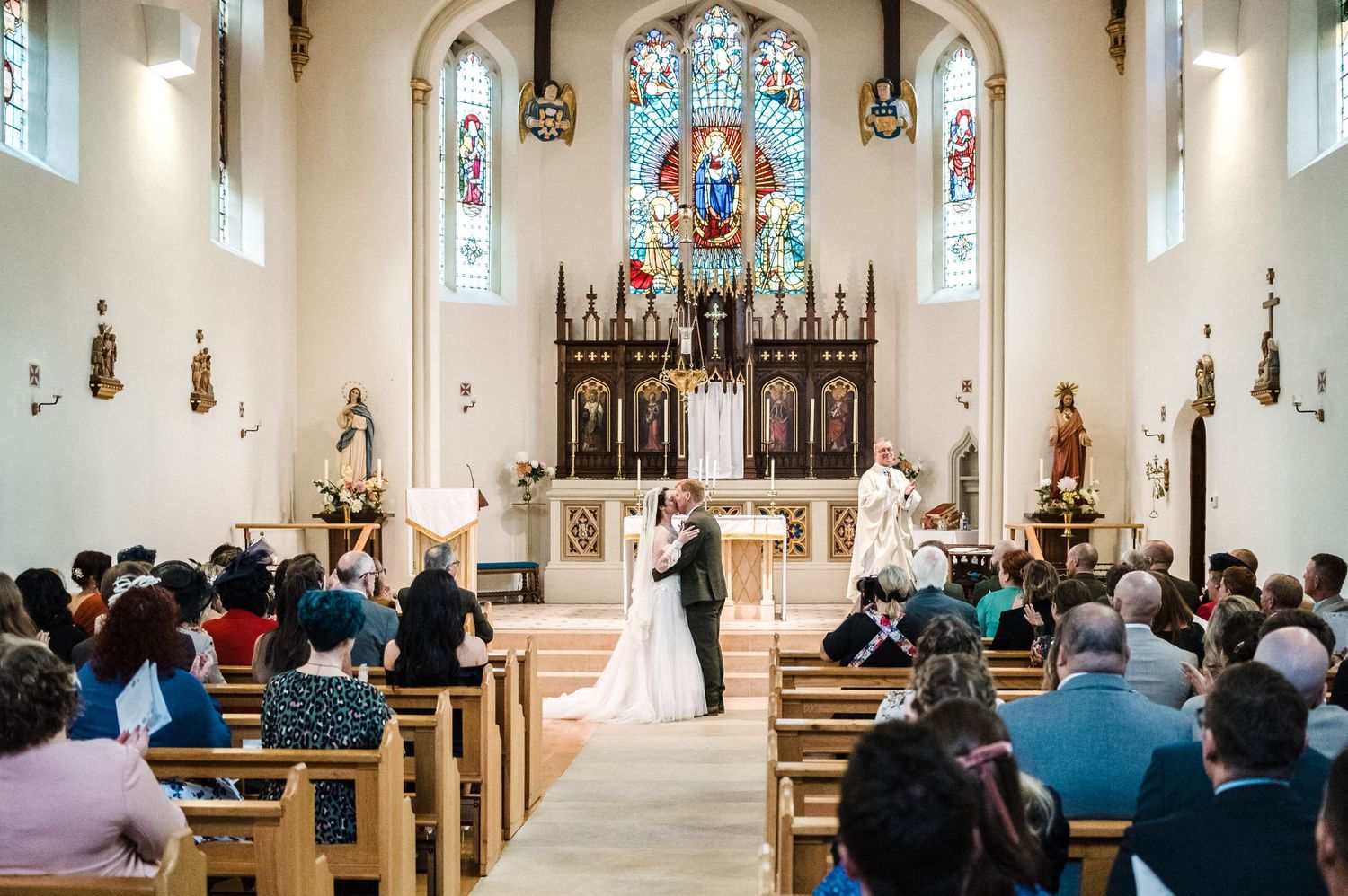 Wide shot of a church wedding ceremony with guests seated in wooden pews.