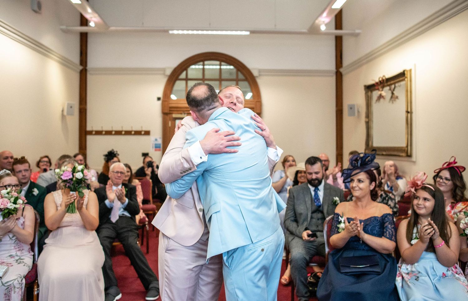Celebratory embrace during wedding ceremony while guests applaud in background.
