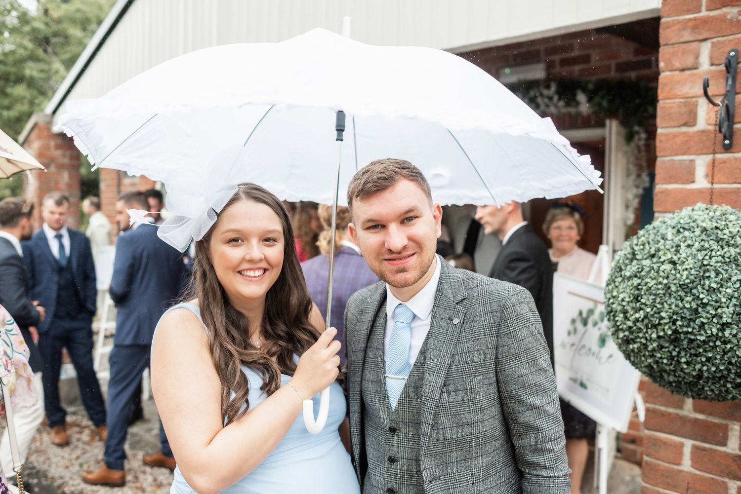 A couple shares a moment under a white umbrella outside a brick building on their wedding day.