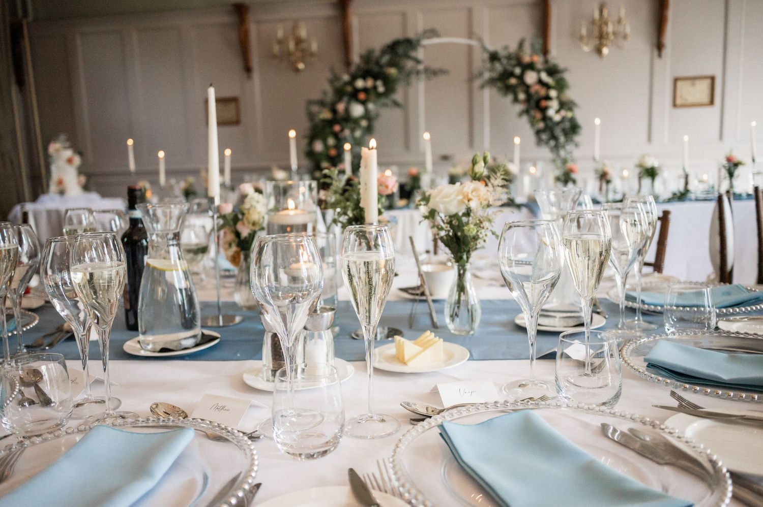 An elegant wedding reception table setting with light blue accents and floral centerpieces.