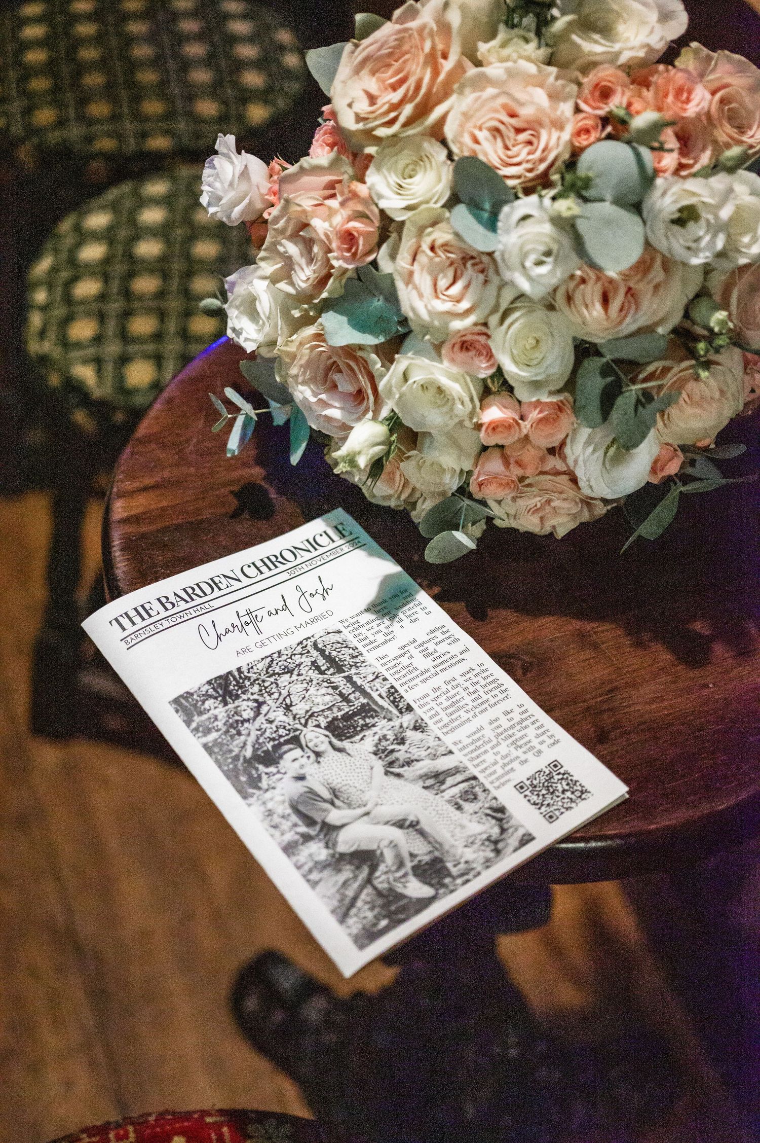 A romantic bouquet of blush and white roses next to a vintage newspaper on a wooden table.