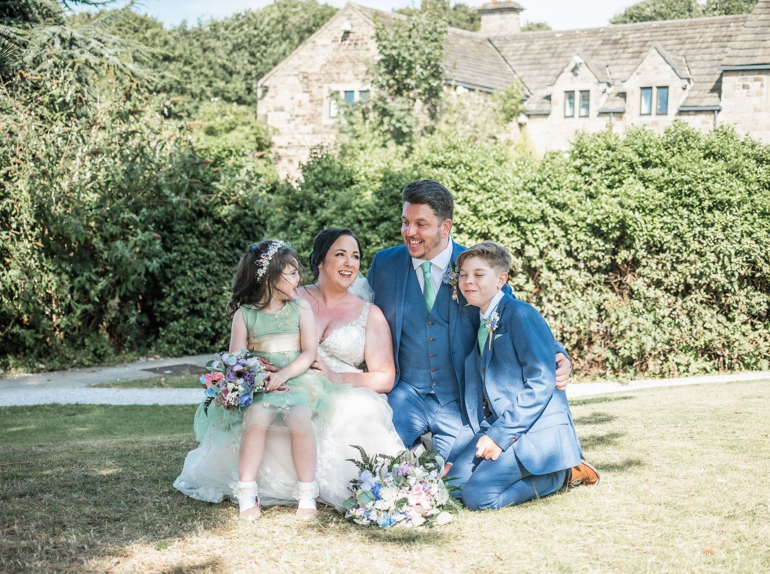 Wedding party poses on lawn in front of stone building with coordinated blue and mint outfits.