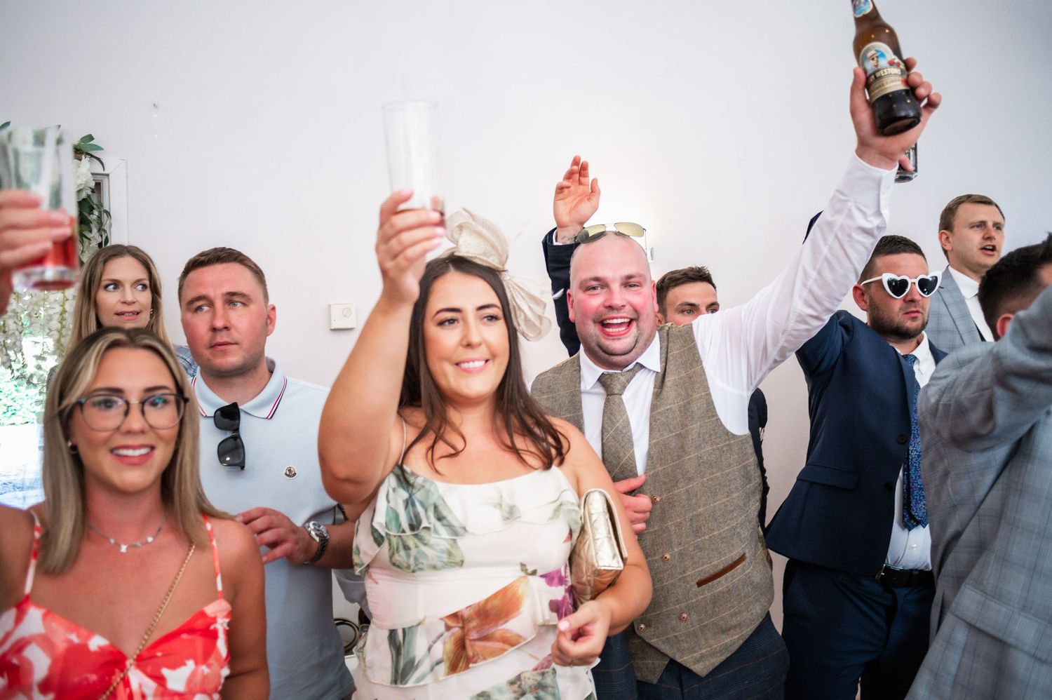 Wedding celebration with guests raising drinks and cheering during indoor reception.
