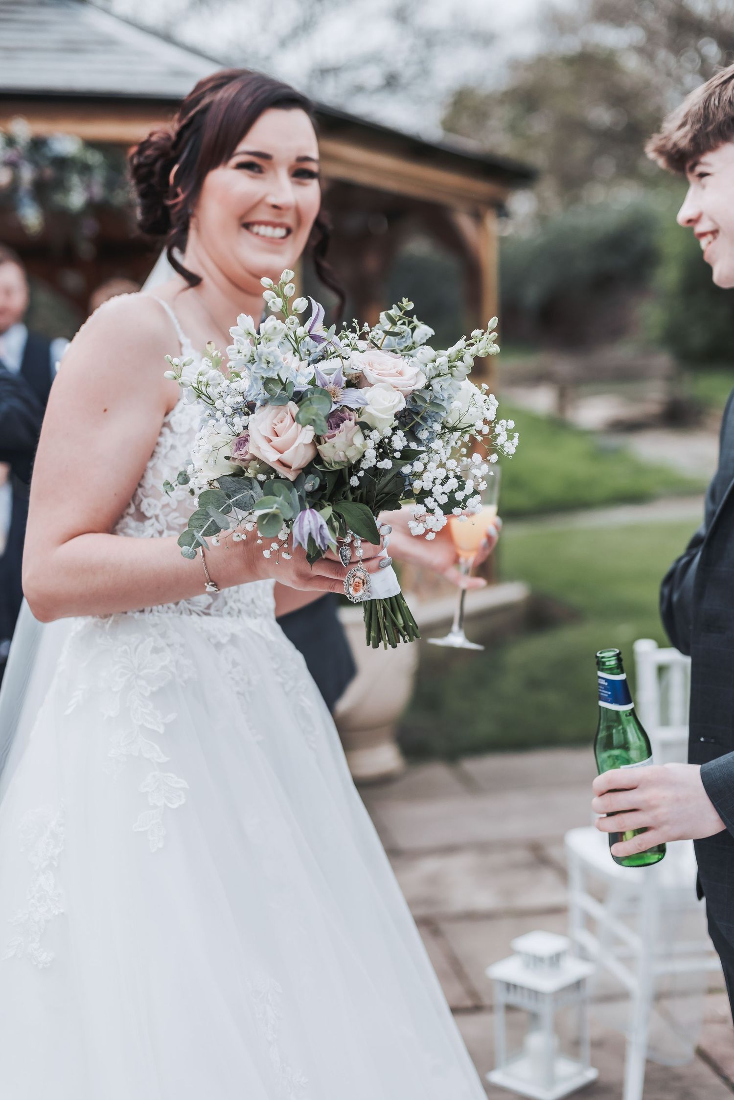 A bride in white dress holds a beautiful bouquet of pink and white flowers at an outdoor ceremony.