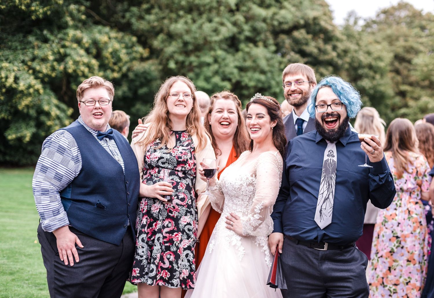 Wedding celebration group photo with guests laughing outdoors.