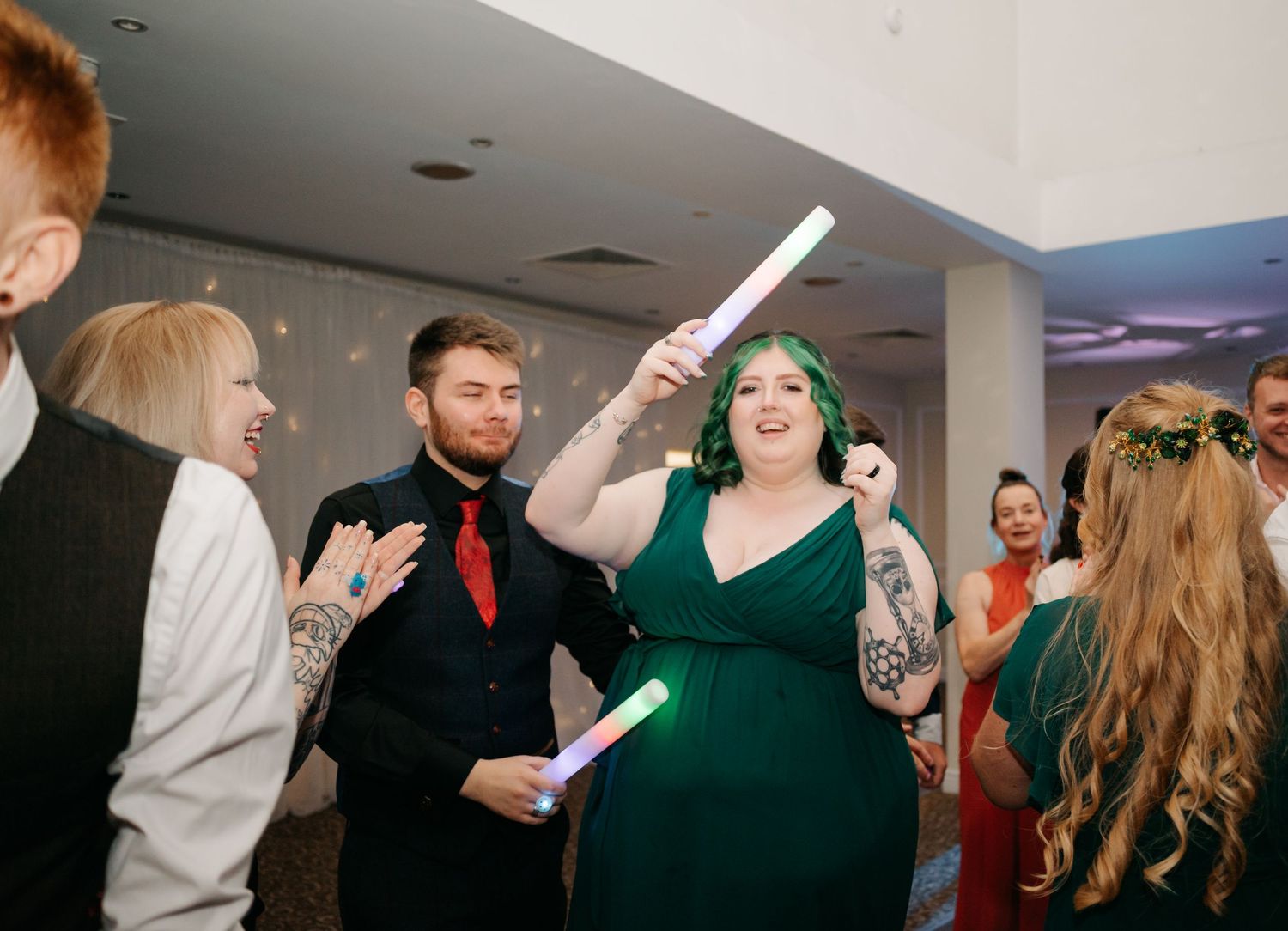 Wedding reception guests dance and celebrate in a dimly lit venue.