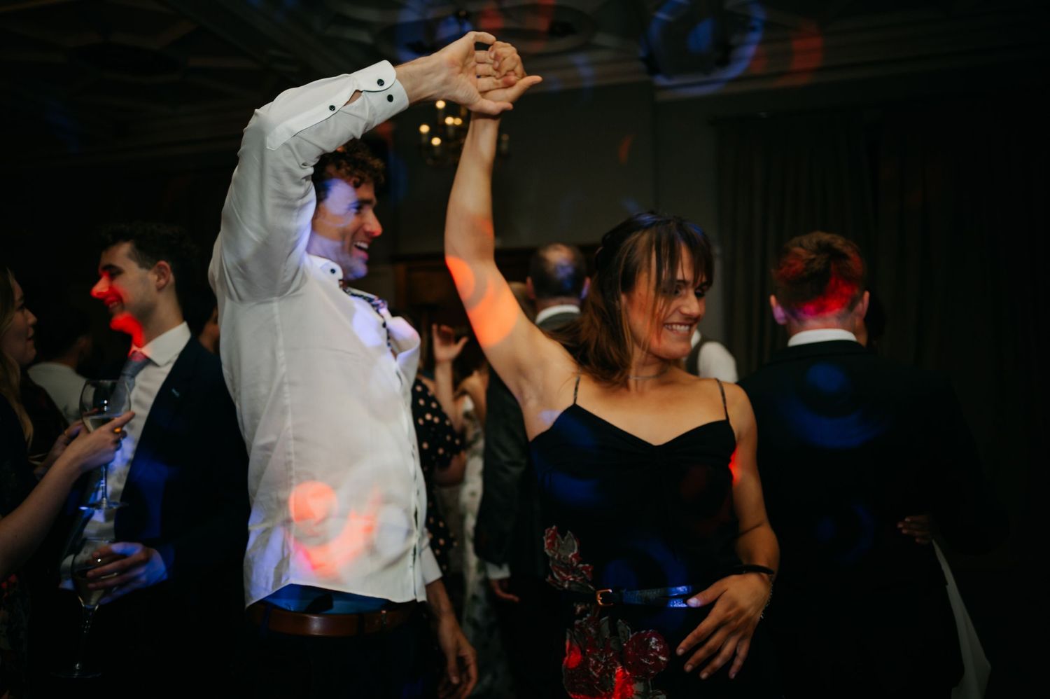 Silhouettes of people dancing at a dimly lit reception with colorful lighting effects.