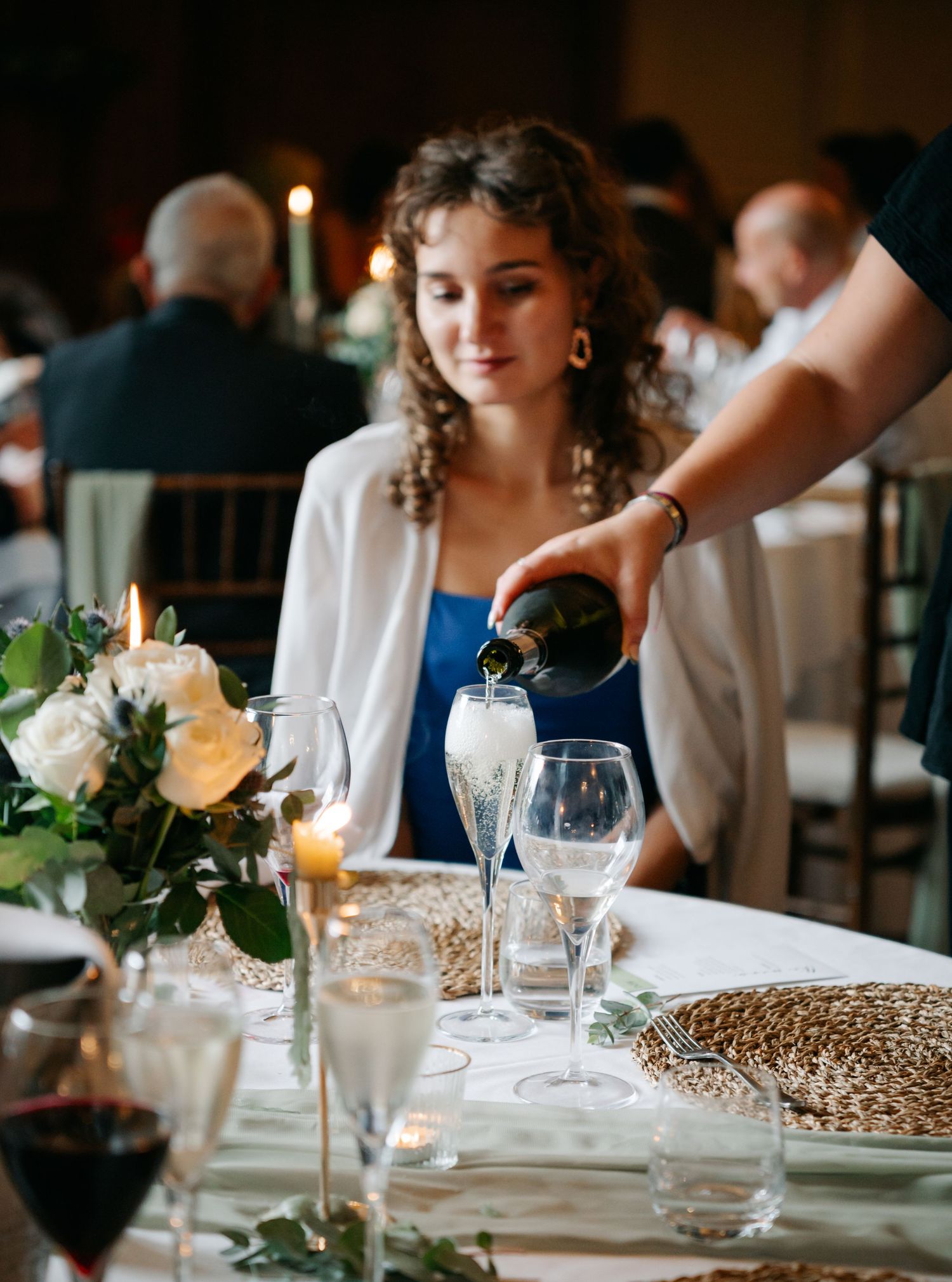 Elegant wedding reception table settings with candlelight, white roses and woven placemats.