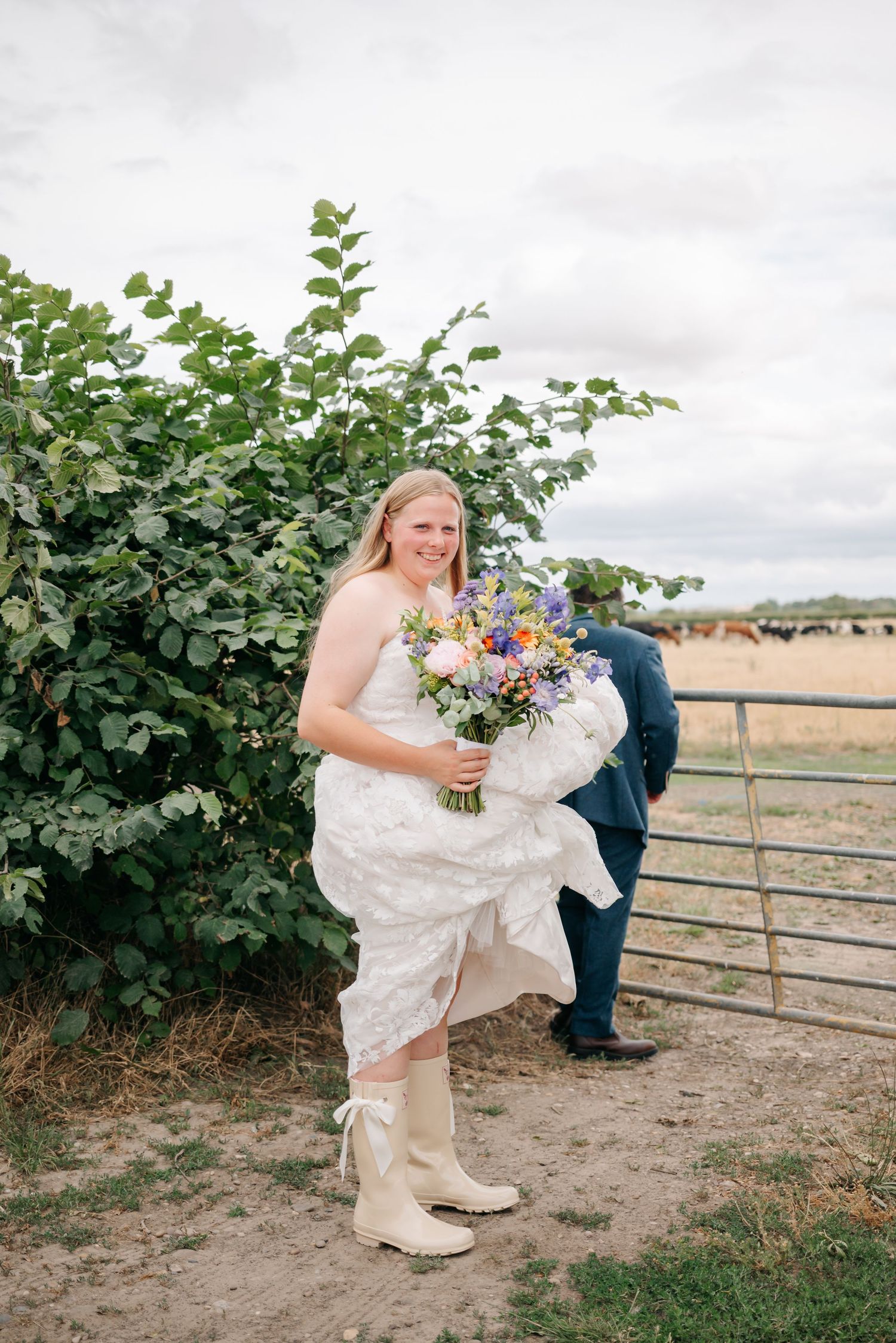 A person in a white dress holding a colorful wildflower bouquet near a rustic fence.