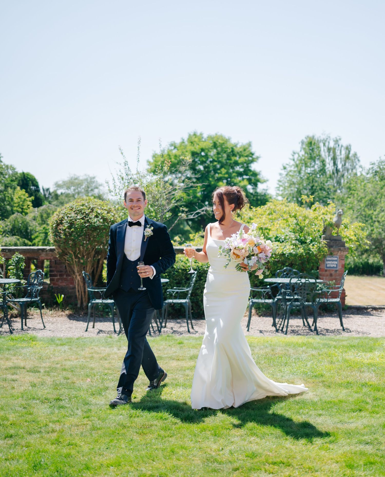 Couple walking and dancing together on grassy lawn during outdoor wedding celebration.