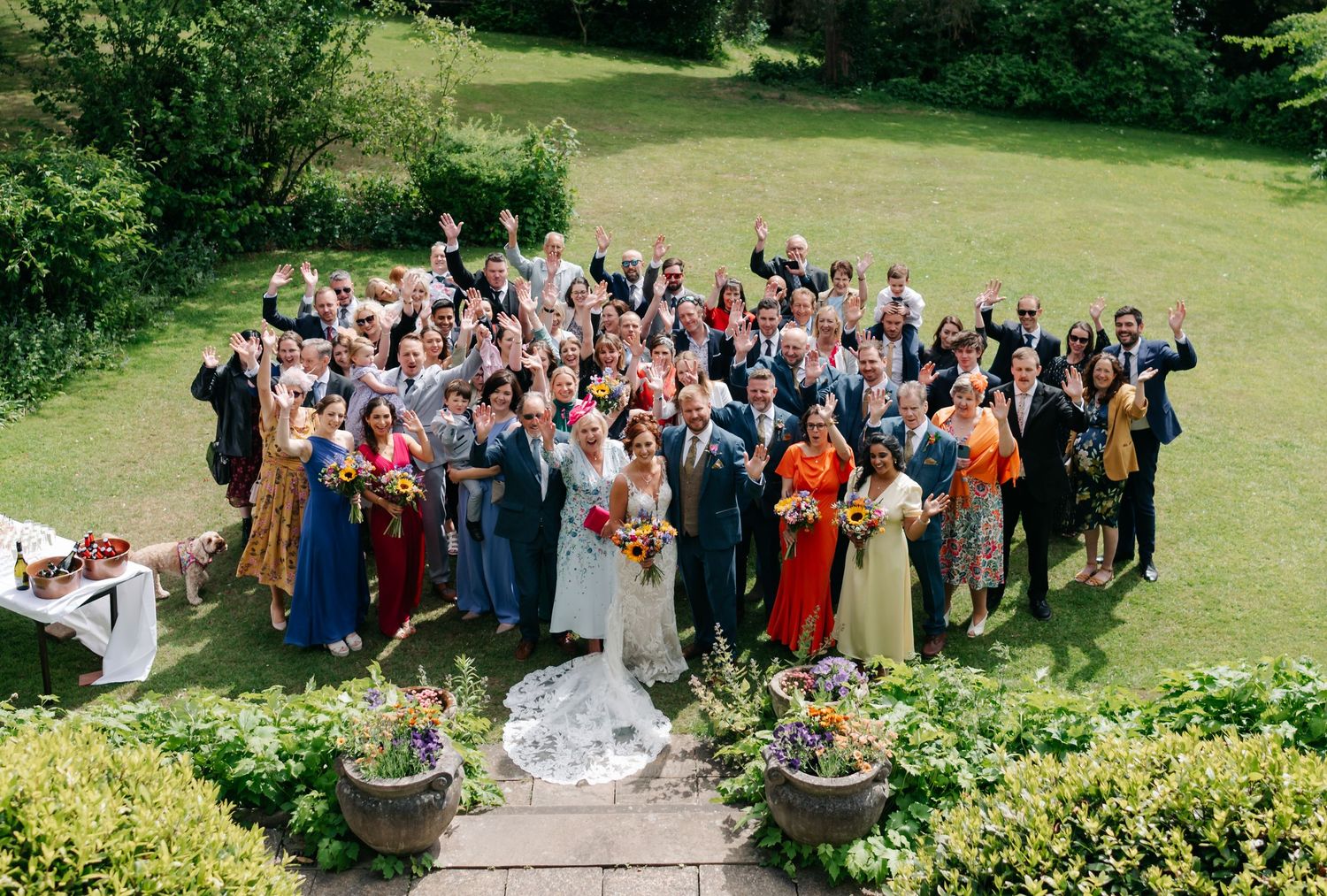 Large wedding party and guests pose for a group photo on a sunny lawn.
