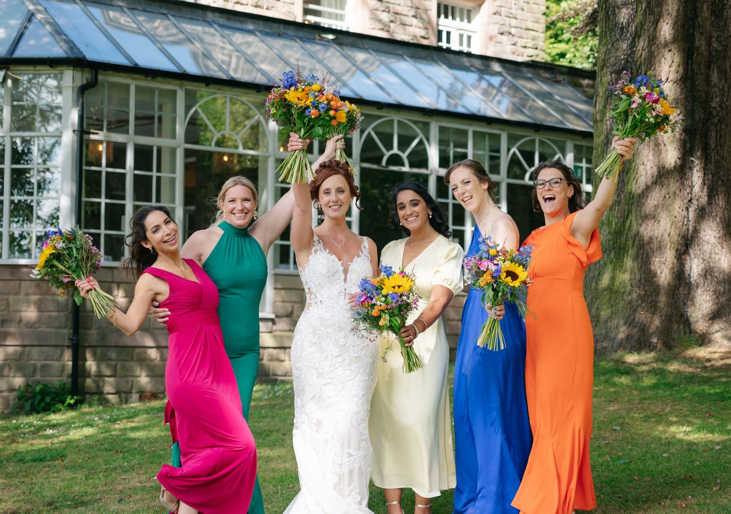 Wedding party in vibrant dresses of pink, blue and orange posing outdoors.