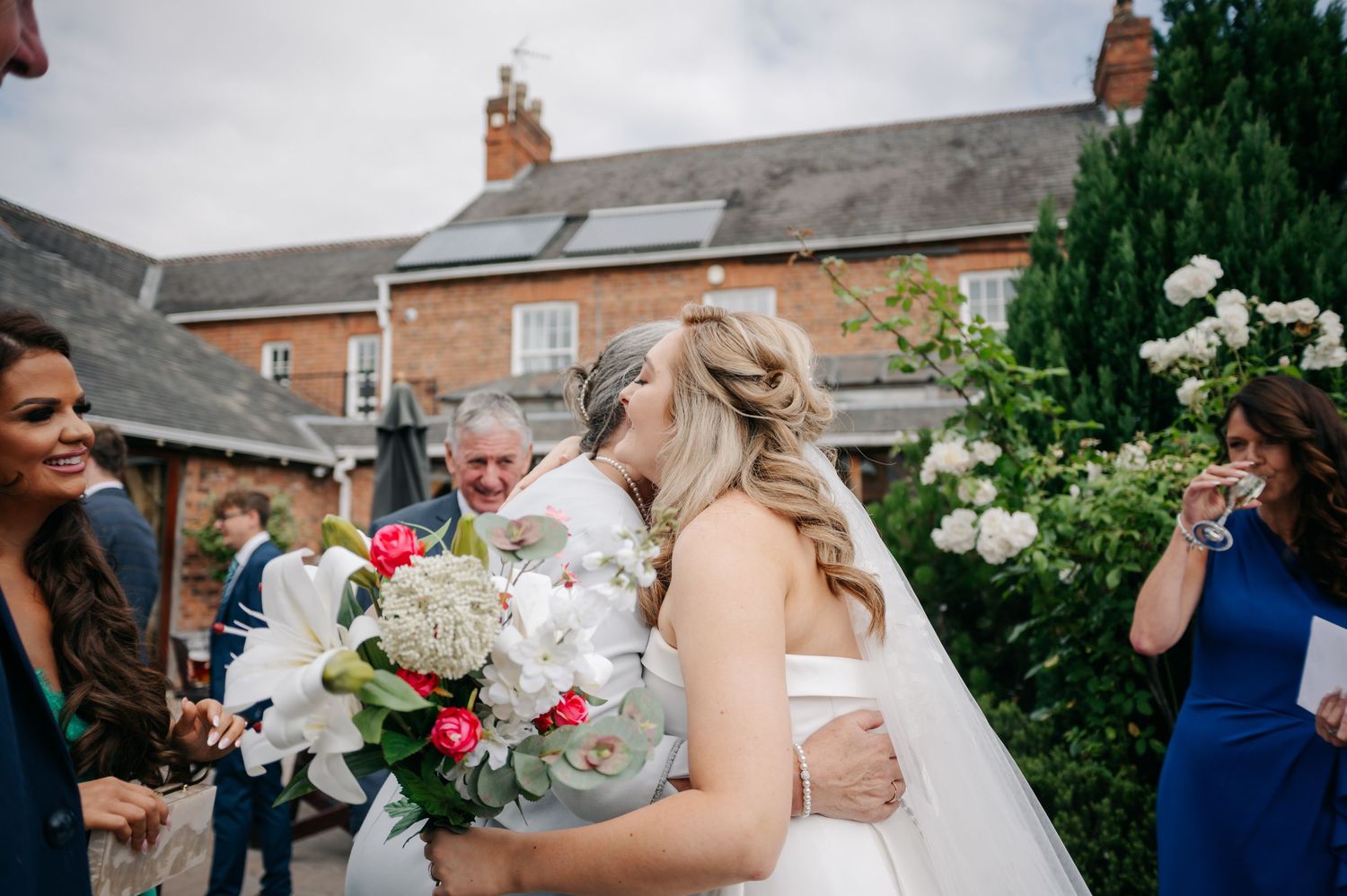 Joyful gathering in a garden with beautiful white floral bouquets against a charming brick house backdrop.