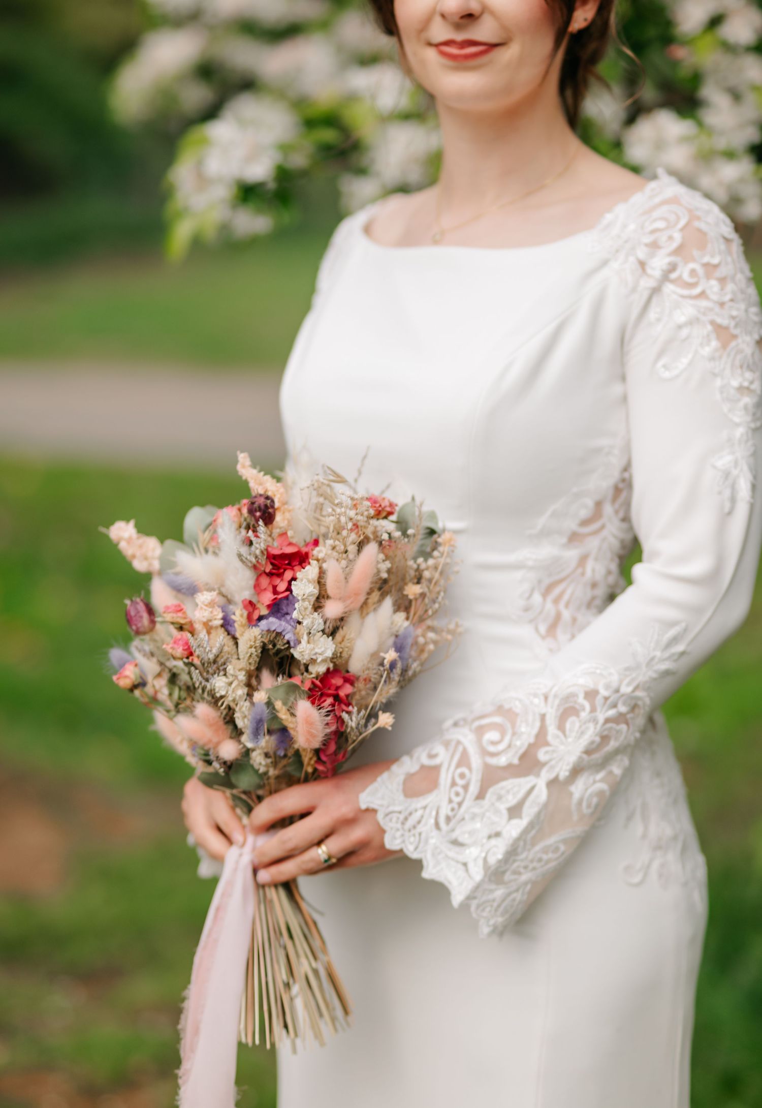 Elegant bridal details showing lace sleeves and a pink and white dried flower bouquet.