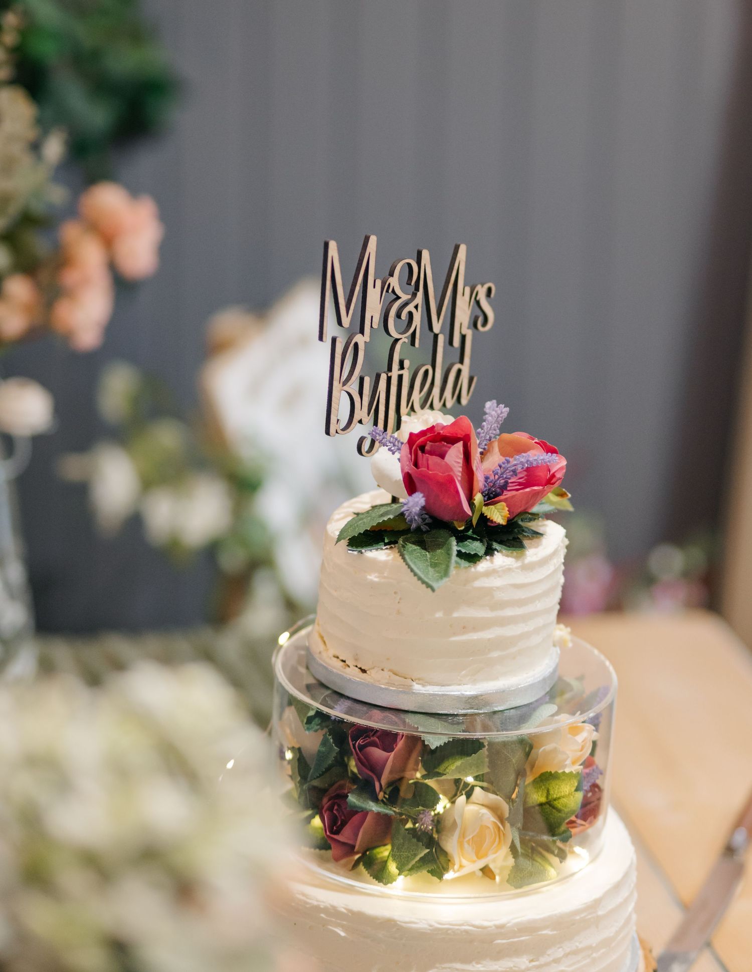 Elegant white wedding cake decorated with fresh flowers and personalized topper.