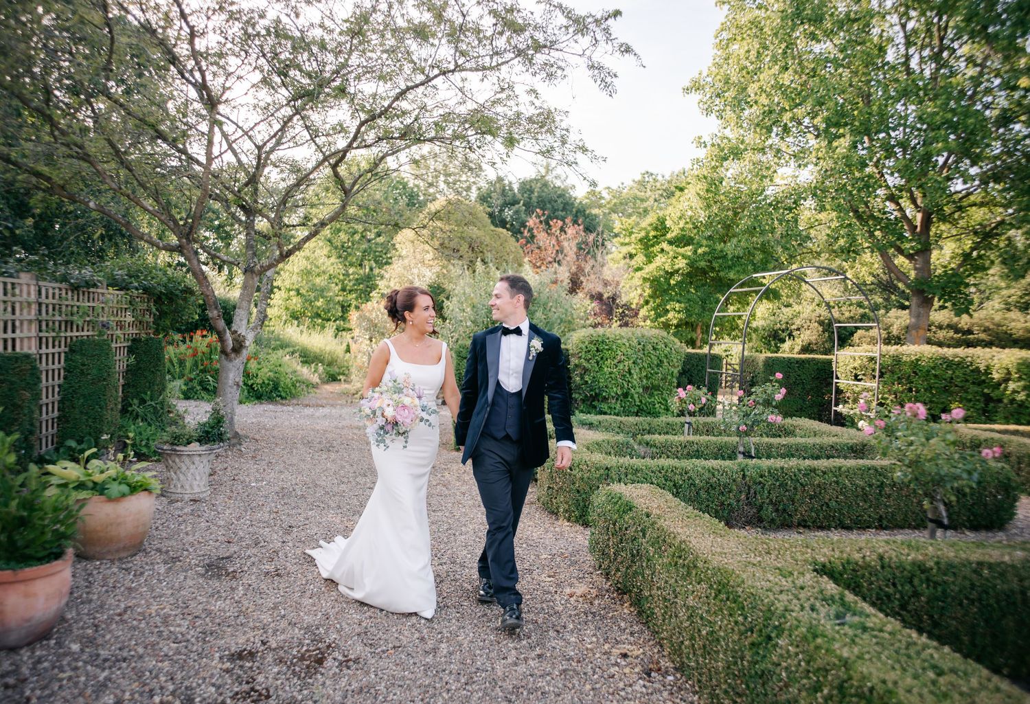 Wedding party walking along garden path surrounded by lush greenery.