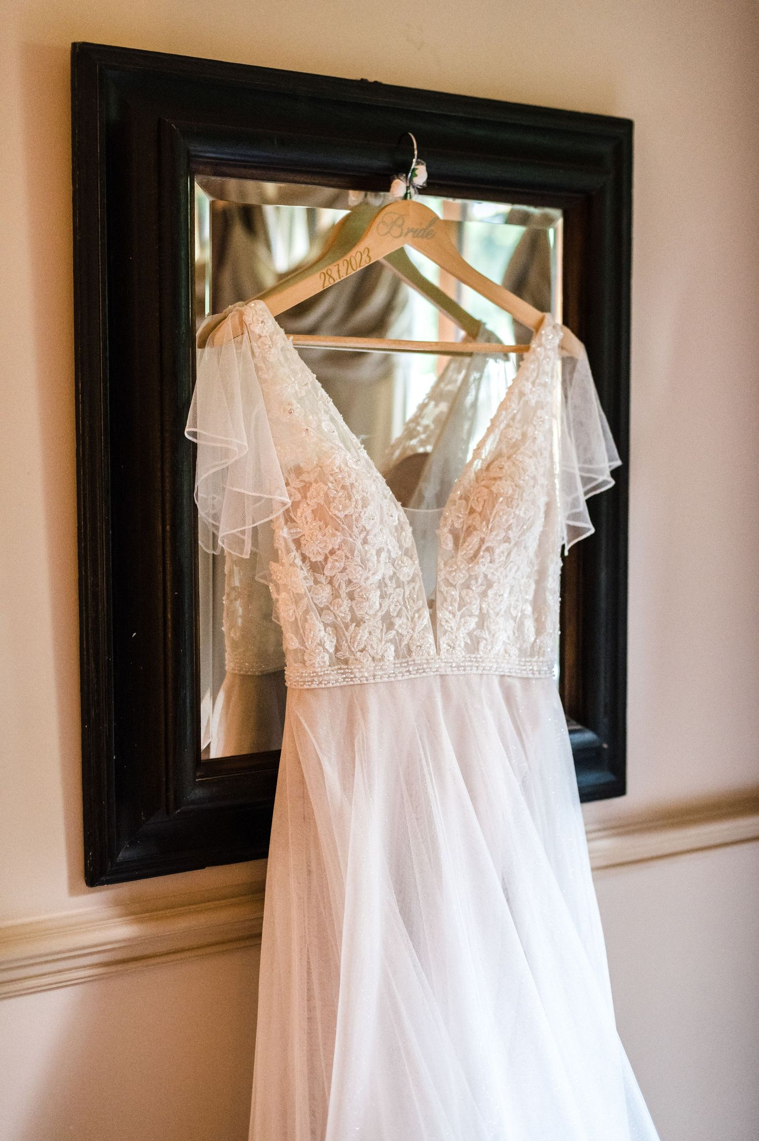 Delicate white lace wedding dress hanging on display against a framed mirror.