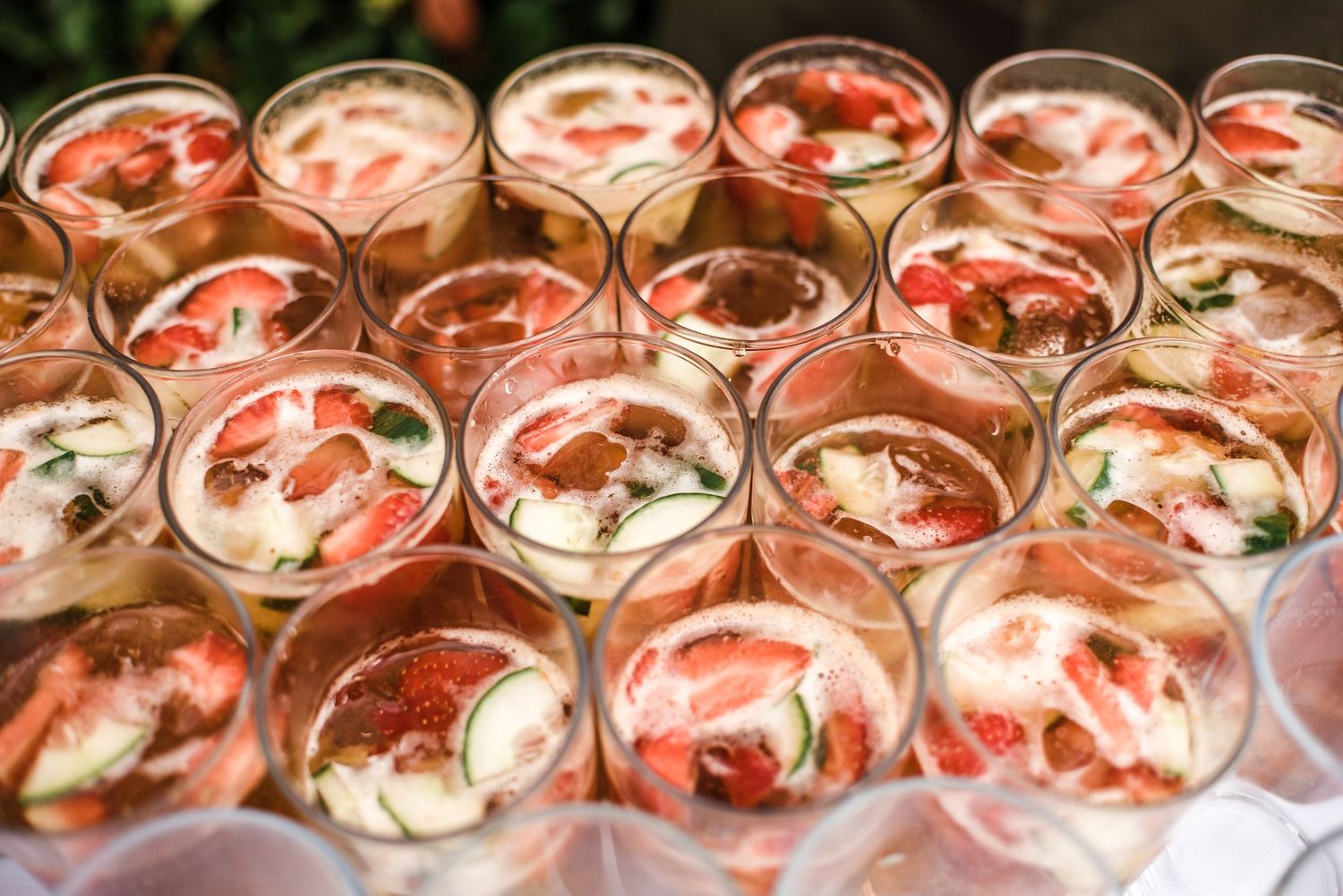 Multiple glasses of pink cocktails garnished with flowers arranged in rows.