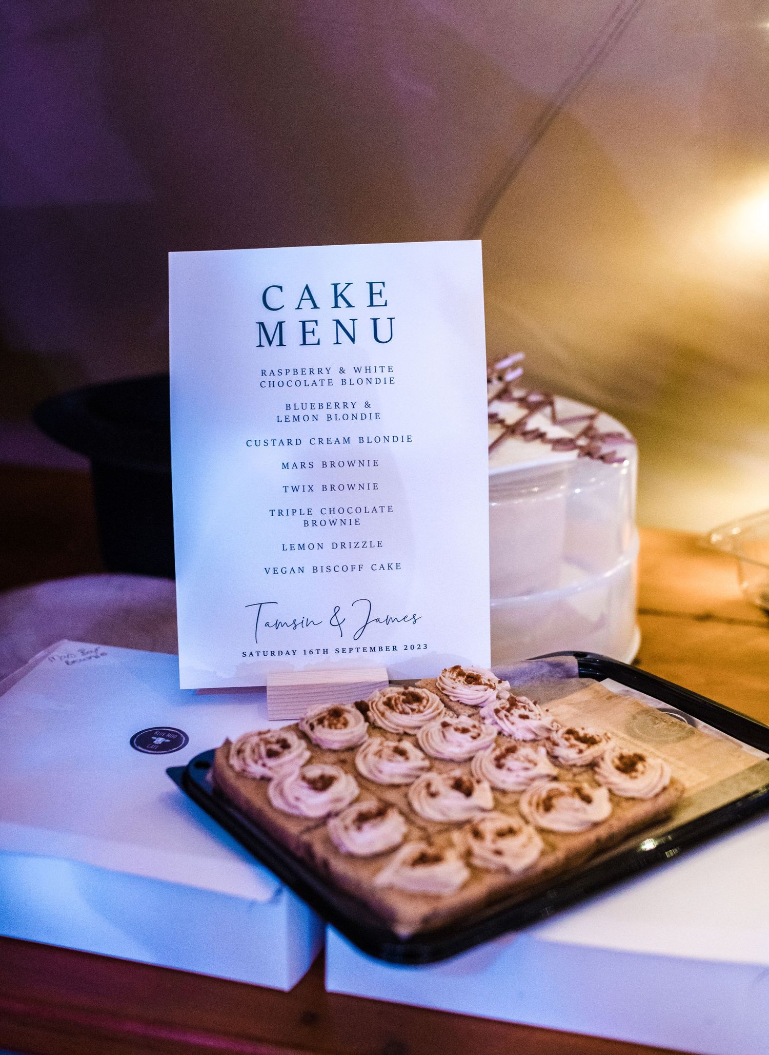 Wedding cake menu card displayed next to fresh baked pastries on a dark surface.