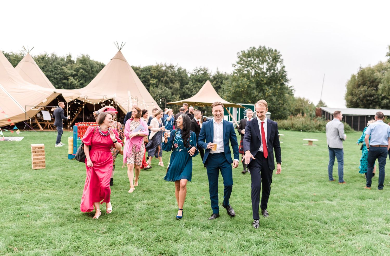 Wedding guests walking across lawn with teepee tents in background.