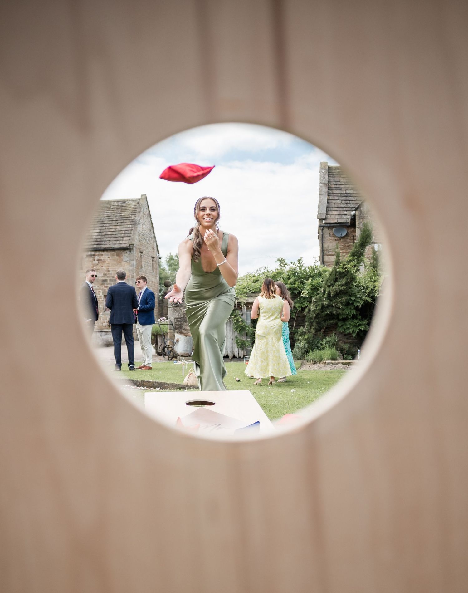 Through a circular window frame, guests play outdoor wedding lawn games.