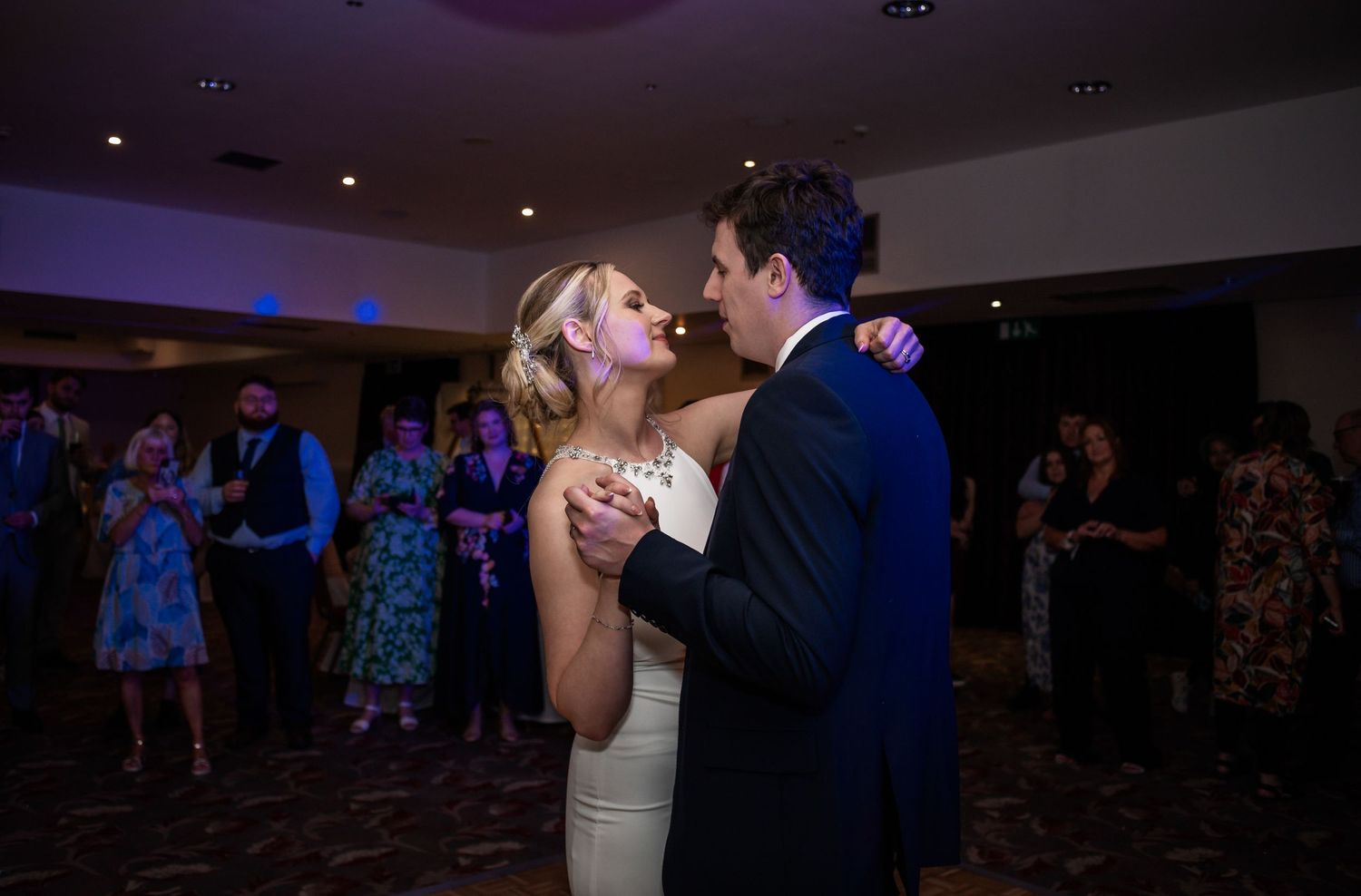 Couple shares their first dance at wedding reception with guests looking on.