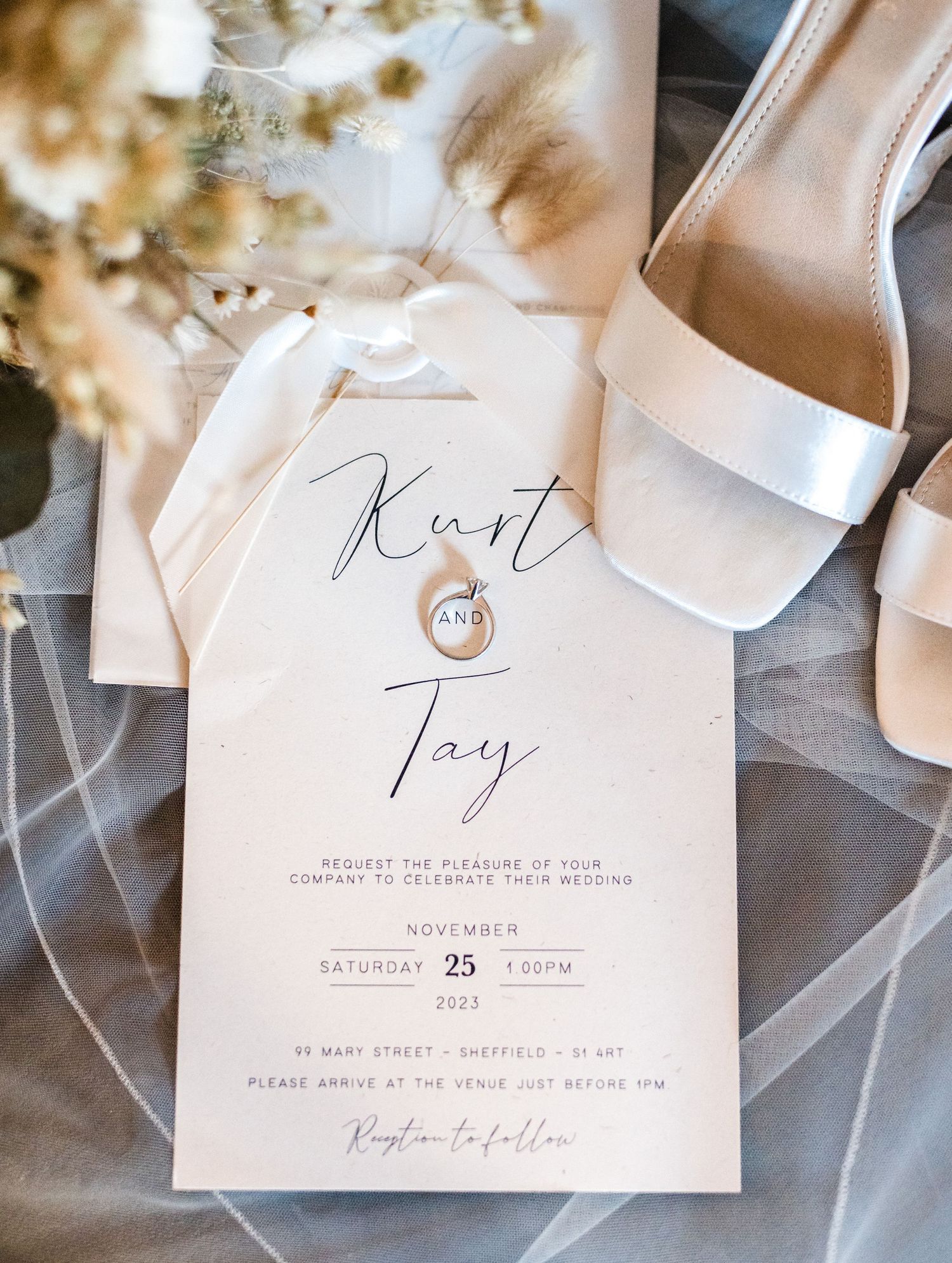 Elegant wedding invitation with white shoes and ring details on veil backdrop.