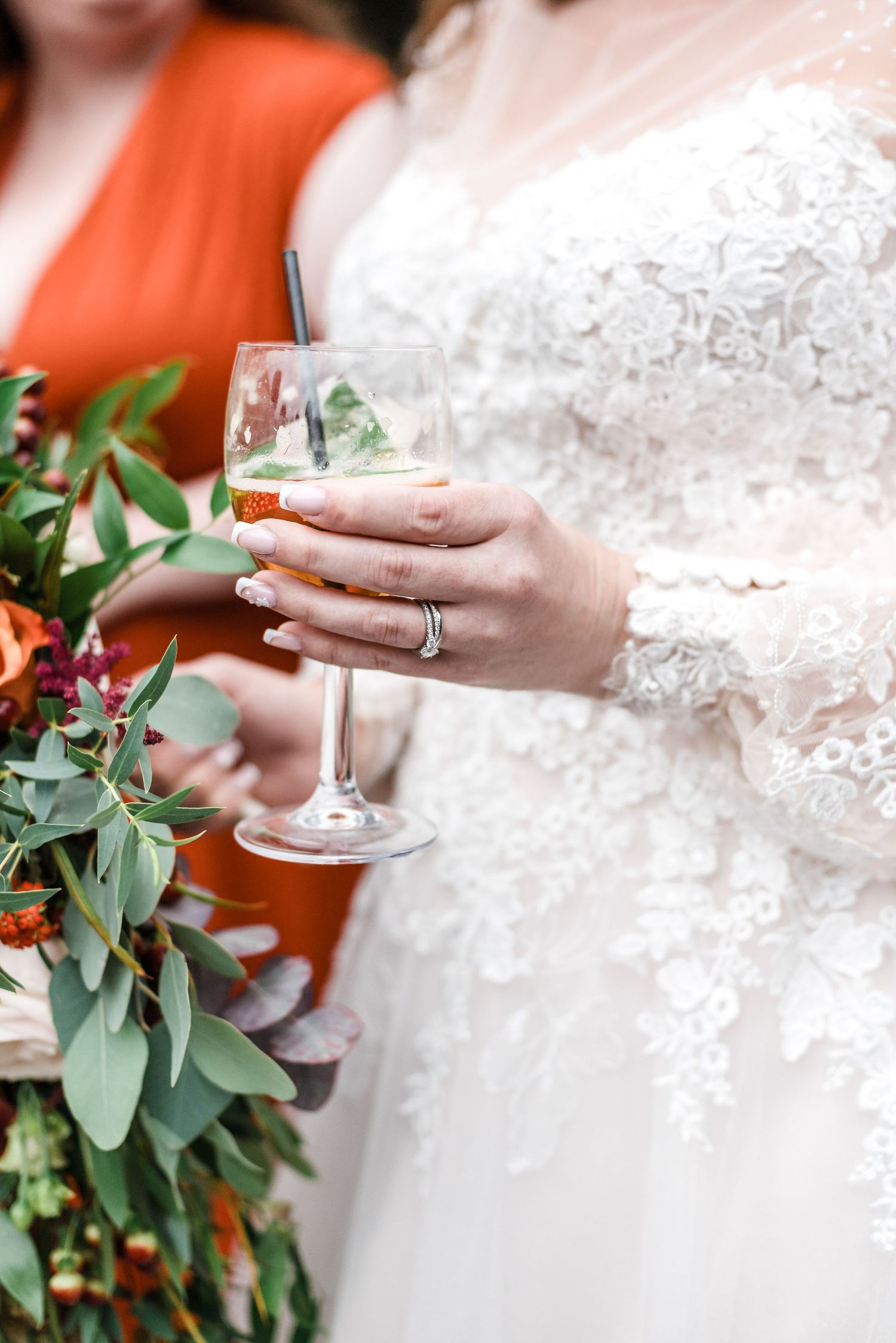 Close-up of bride holding wine glass with wedding ring and floral bouquet.