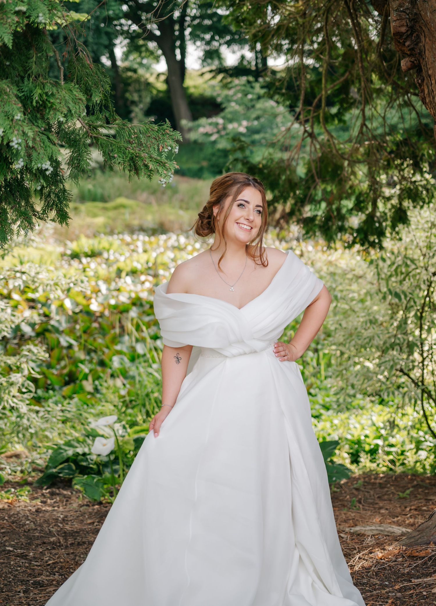 Ethereal wedding scene with flowing white gown photographed under overhanging trees in a lush garden setting.